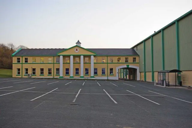 Okell’s brewery at Kewaigue, a long yellow and green building with a white-columned entrance and a large car park in front