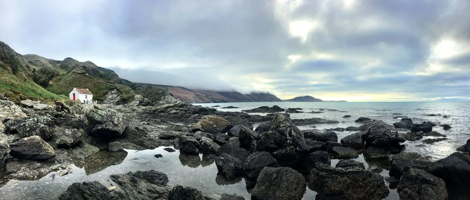 Niarbyl on the west coast under low grey cloud, with the whitewashed cottage, black rocks and rock pools, and the hills of the south-west in mist
