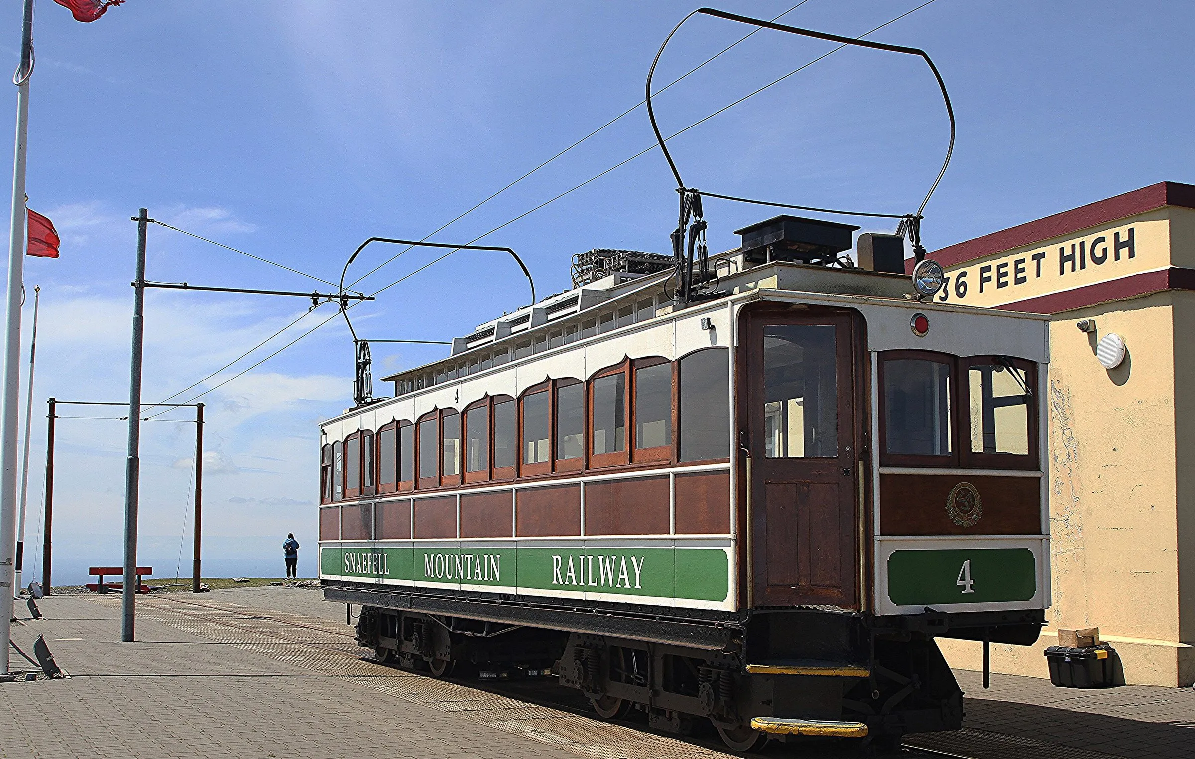 A green and varnished-wood Snaefell Mountain Railway tram at the summit station under a bright blue sky