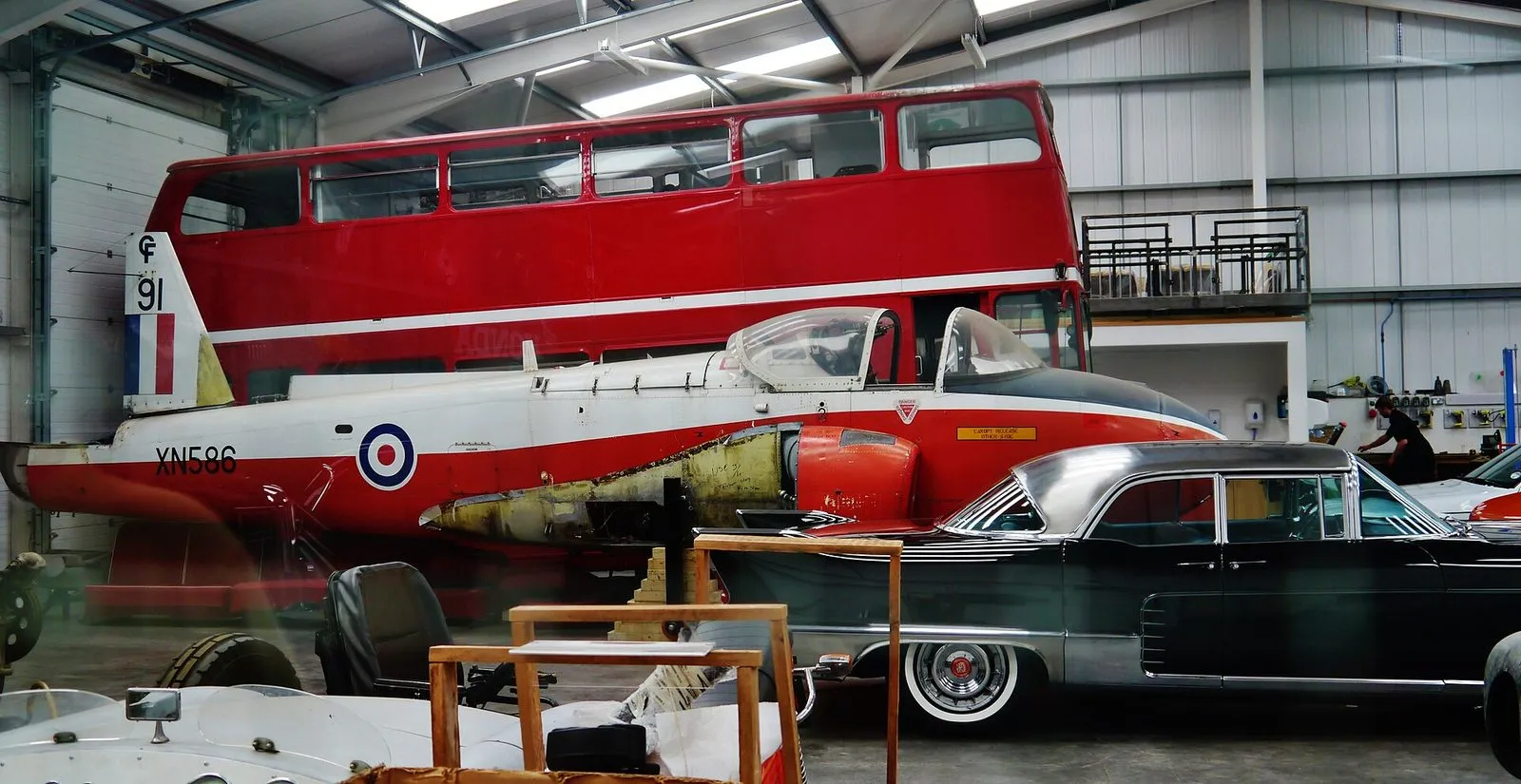 Inside the Isle of Man Motor Museum at Jurby: a red and white RAF jet trainer in front of a red double-decker bus, with a vintage black saloon car alongside
