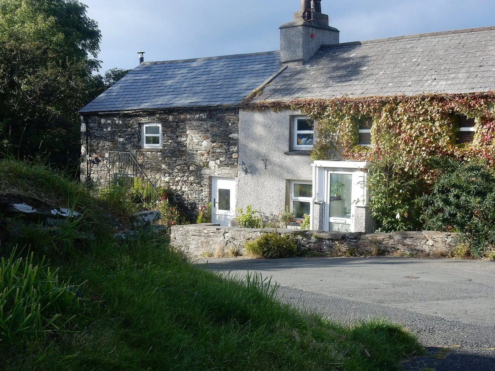 A whitewashed and stone cottage in Glen Maye, with a slate roof and ivy on the wall, beside a quiet lane