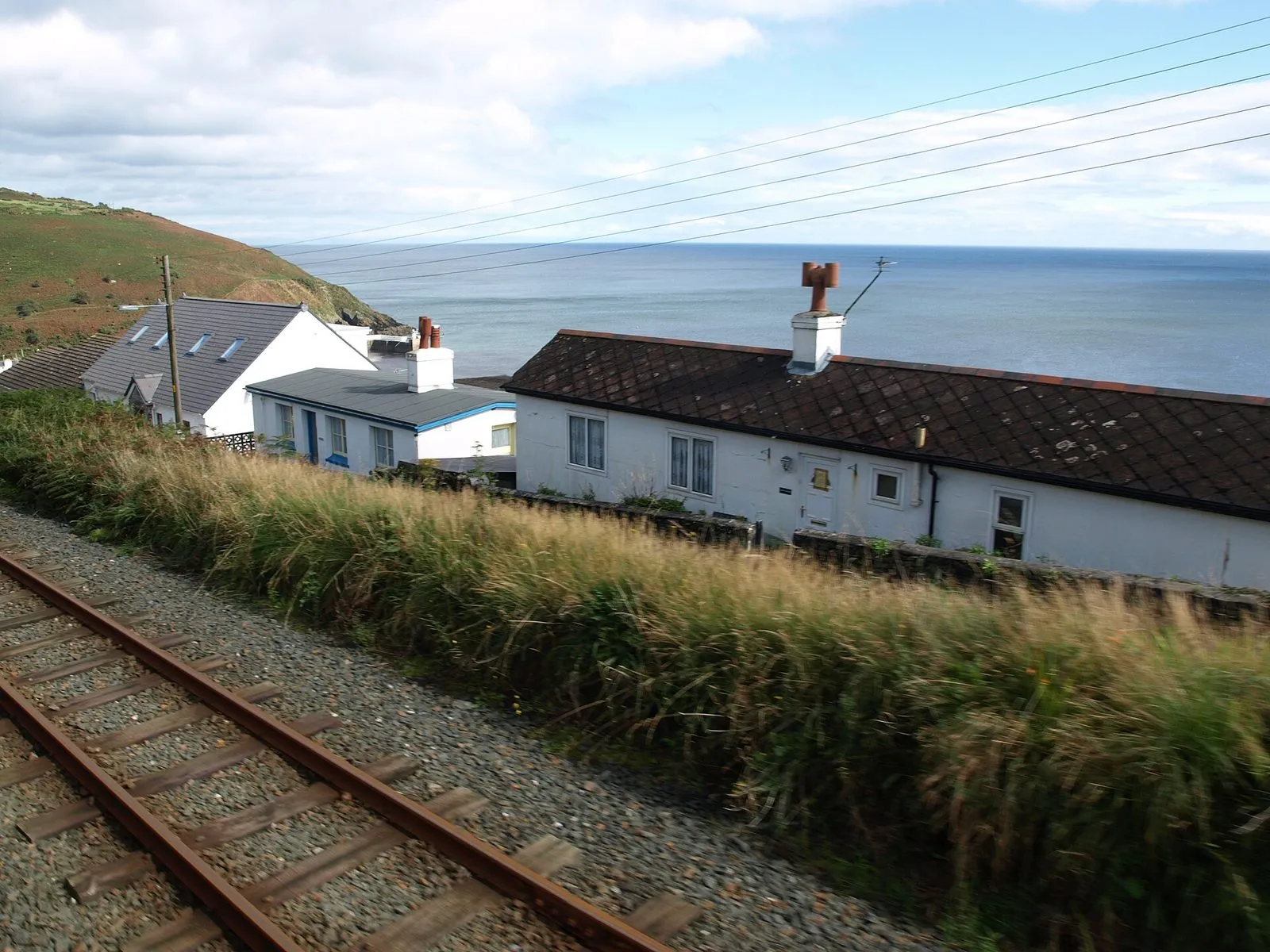 Whitewashed cottages with slate roofs beside the railway line above Laxey, with the Irish Sea behind
