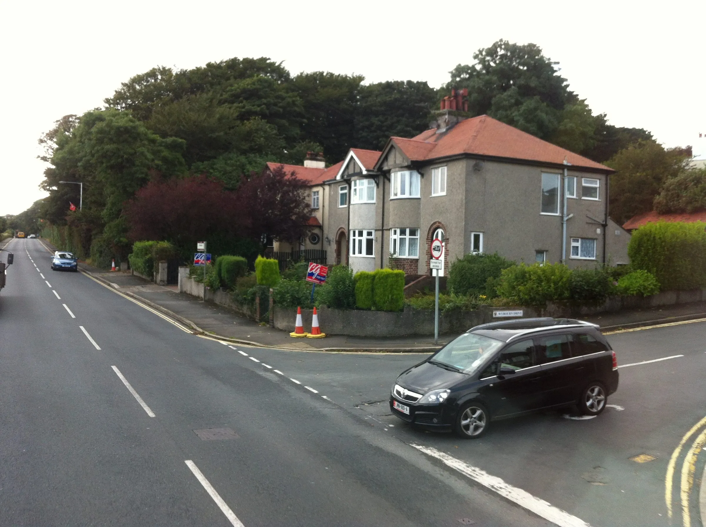 A pair of 1930s pebble-dashed semi-detached houses with red-tiled roofs on a tree-lined road in Onchan
