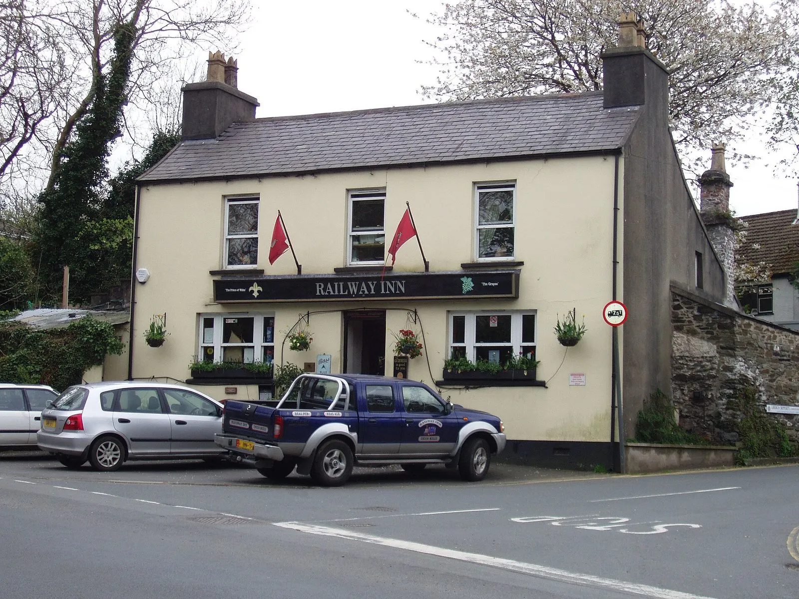 The Railway Inn at Union Mills, a cream-painted pub with red flags, beside the road