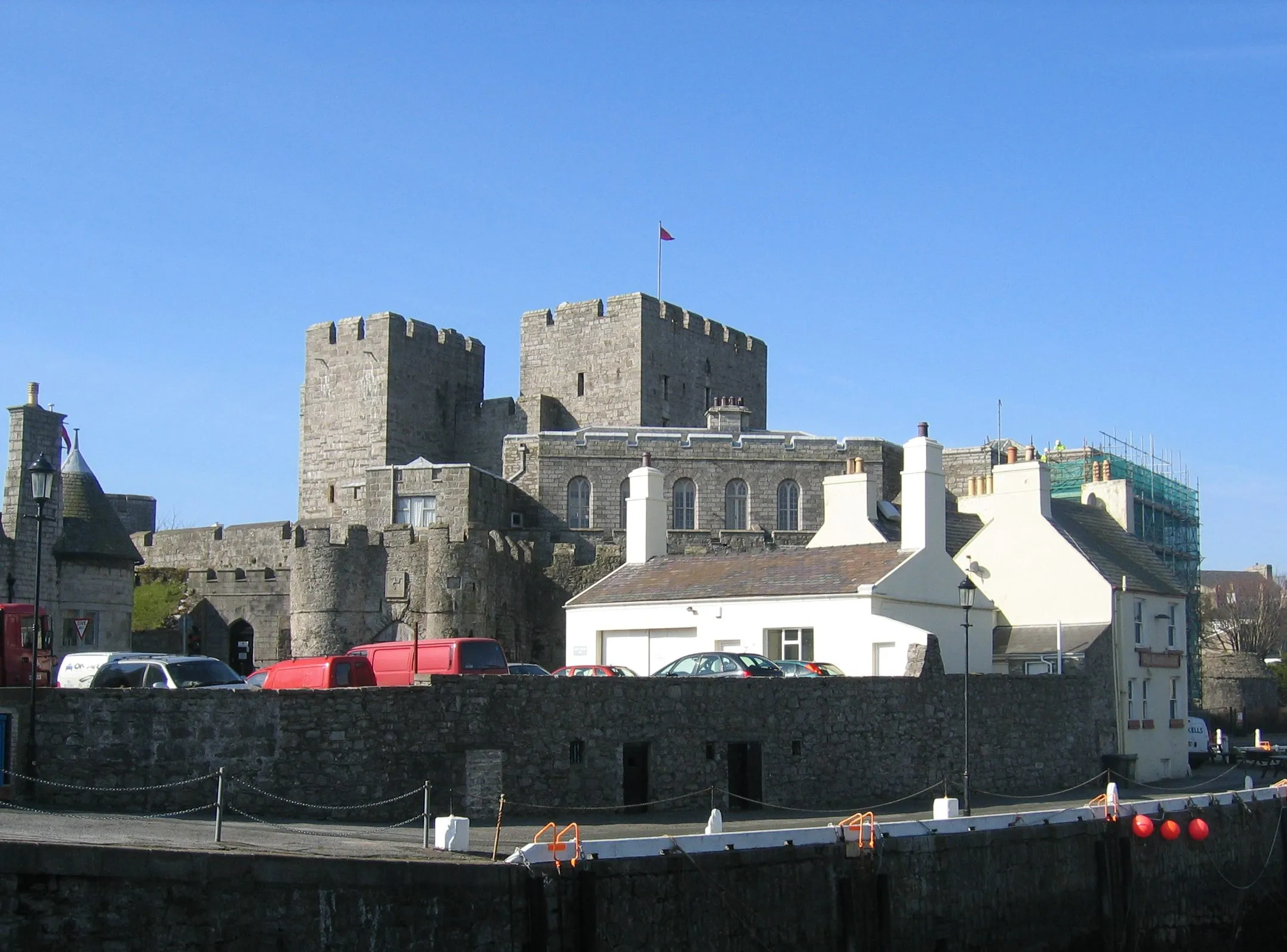 Castle Rushen's grey limestone towers rising behind the white cottages and harbour wall of Castletown under a clear blue sky