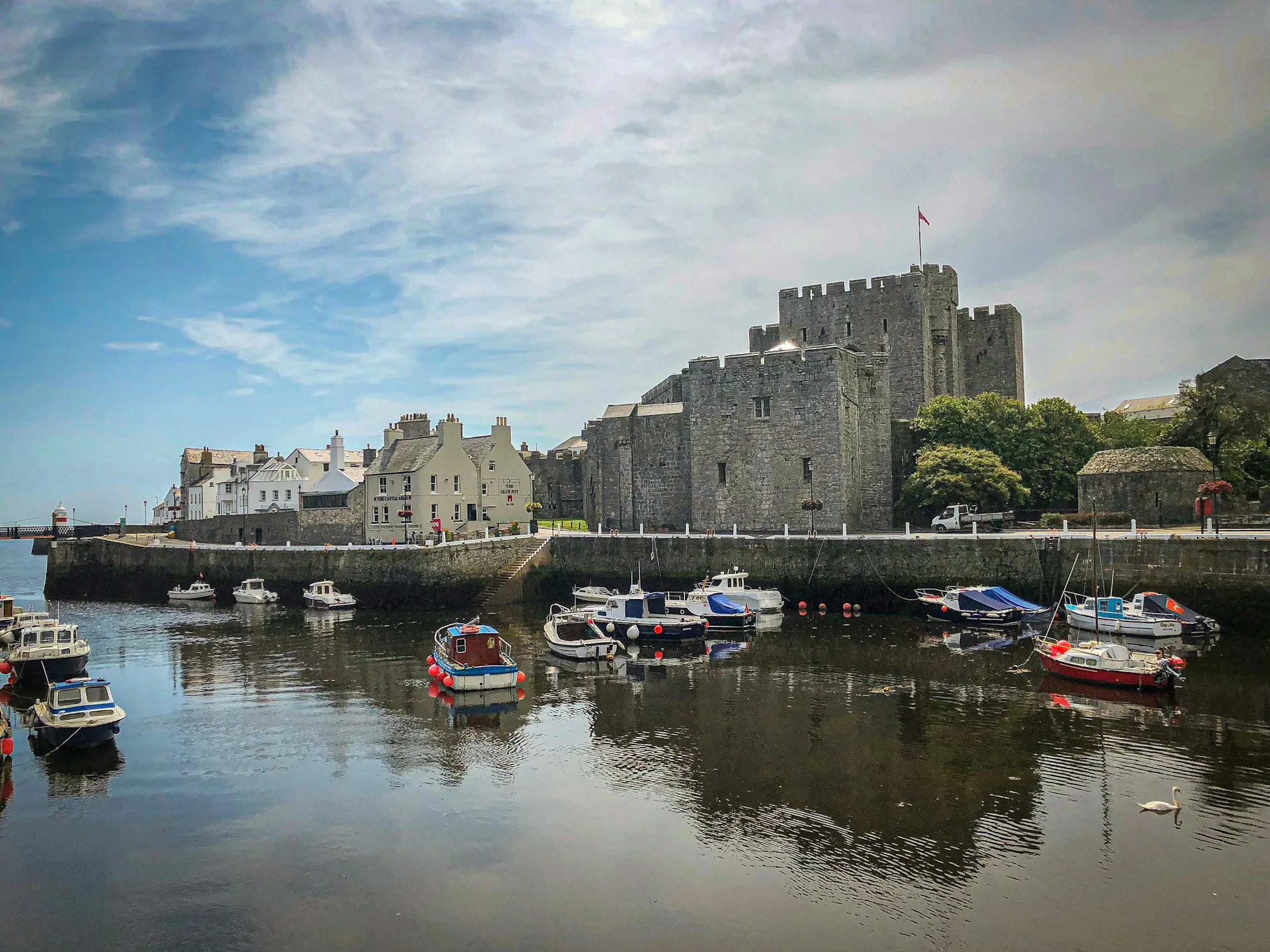 Castle Rushen's grey limestone keep rising above Castletown's inner harbour, with small boats moored on still water and white houses along the quay