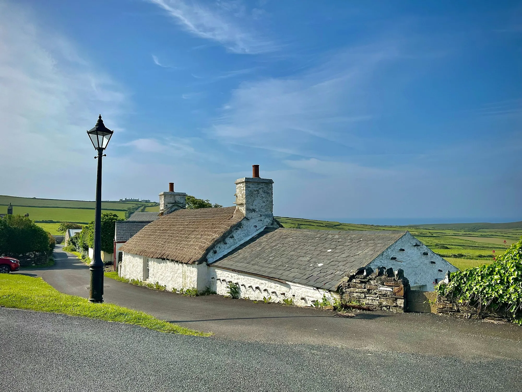 A whitewashed thatched cottage by the lane in Cregneash, with fields running off behind it