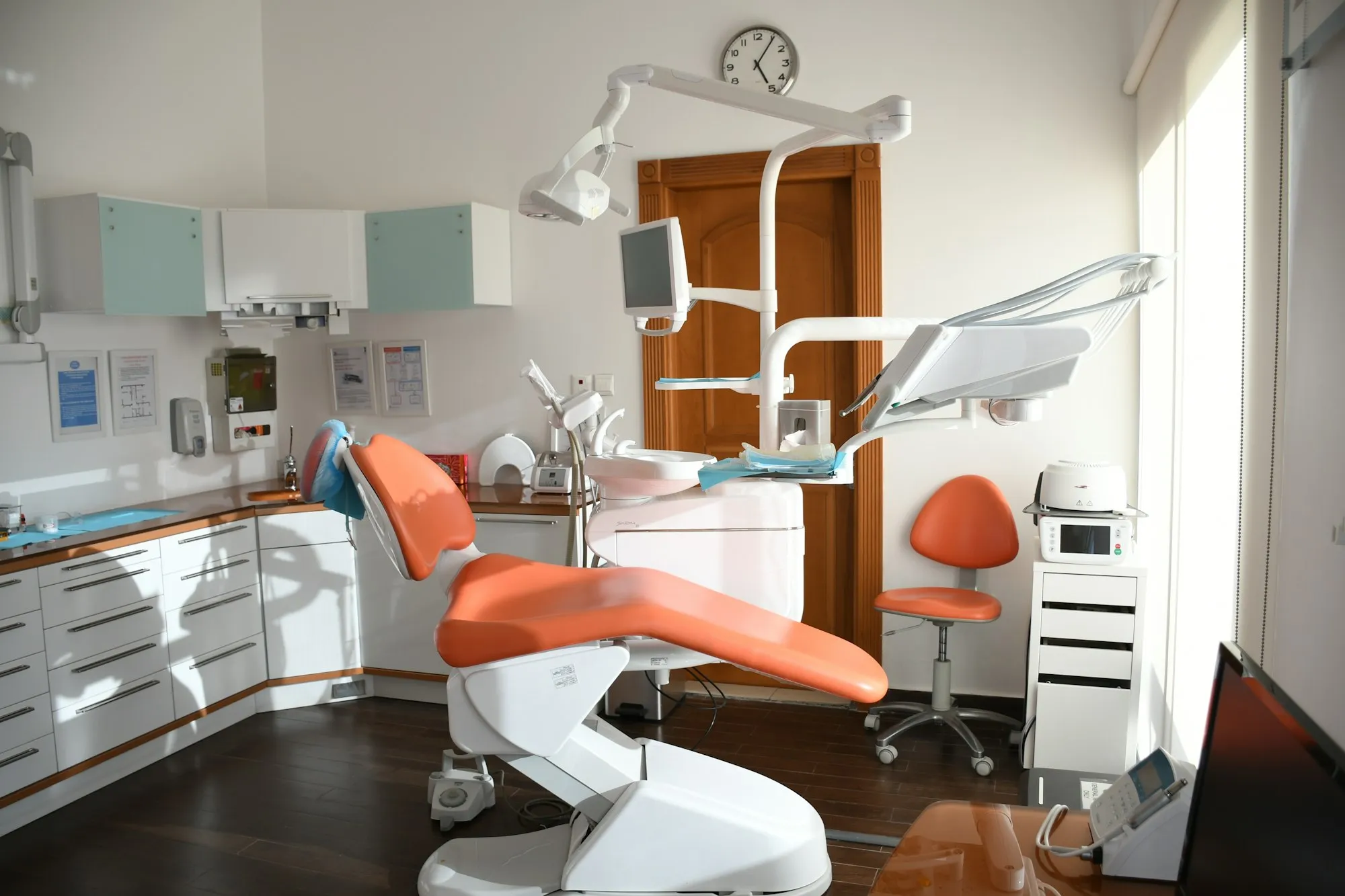 An empty dental surgery with an orange dental chair under the overhead lamp