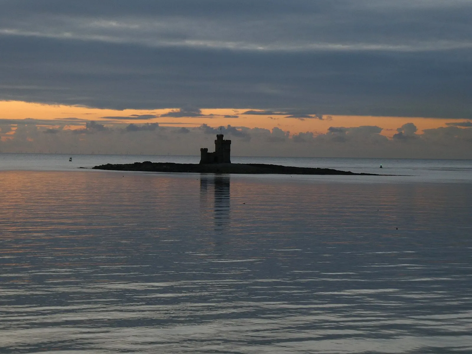 The Tower of Refuge silhouetted on its rock in Douglas Bay at sunrise, with the sky orange behind it and the sea flat calm