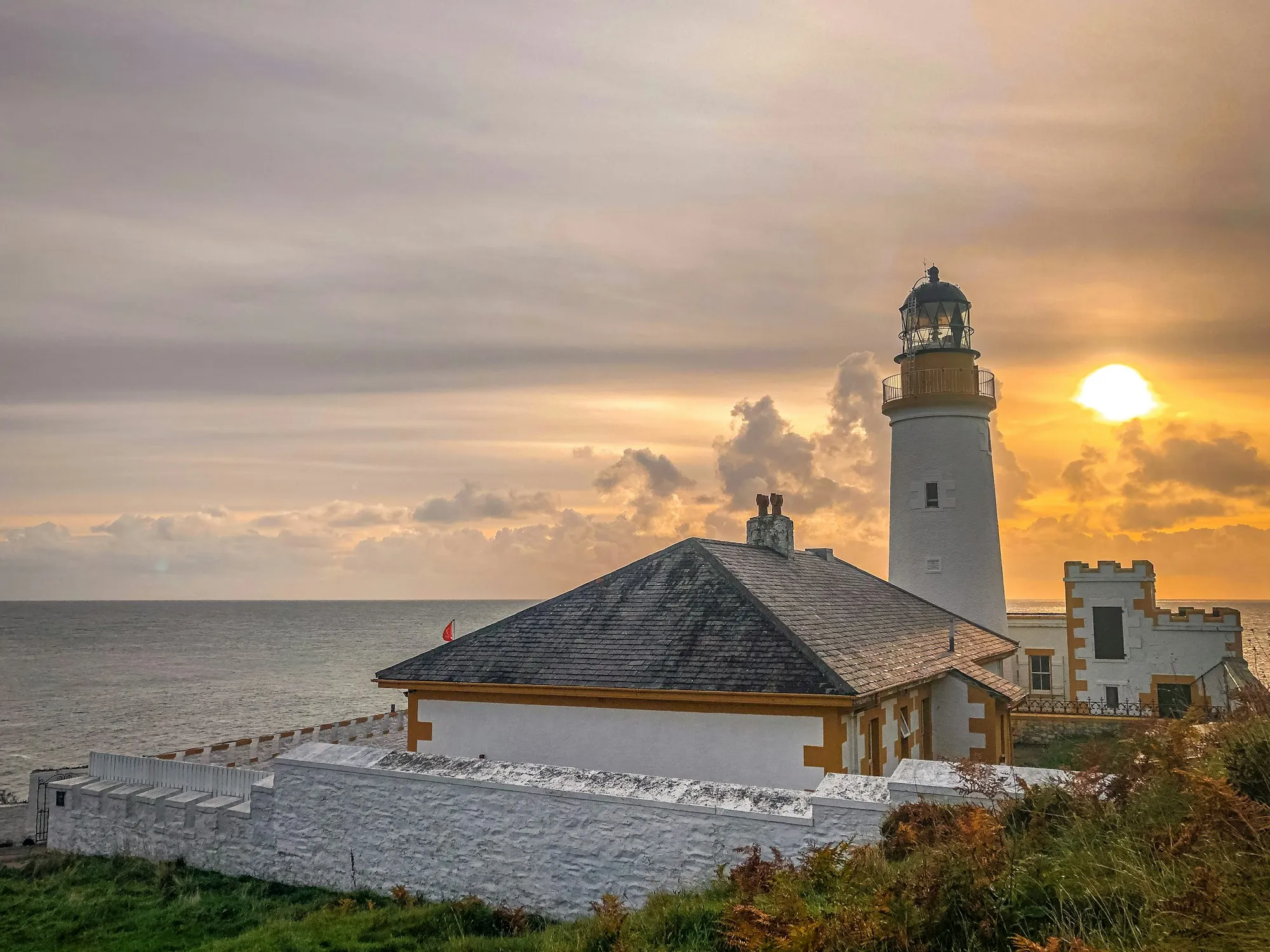 Douglas Head Lighthouse at sunset, its white tower and keeper's cottage on the headland above the sea