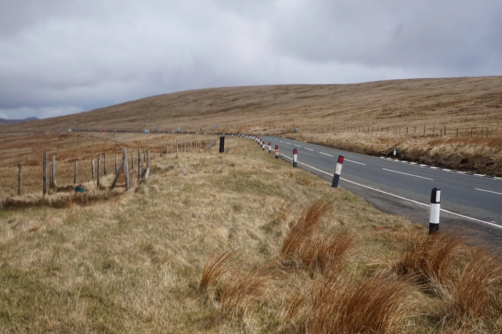 The A18 Mountain Road curving across bare brown moorland under a grey sky, lined with black and white marker posts