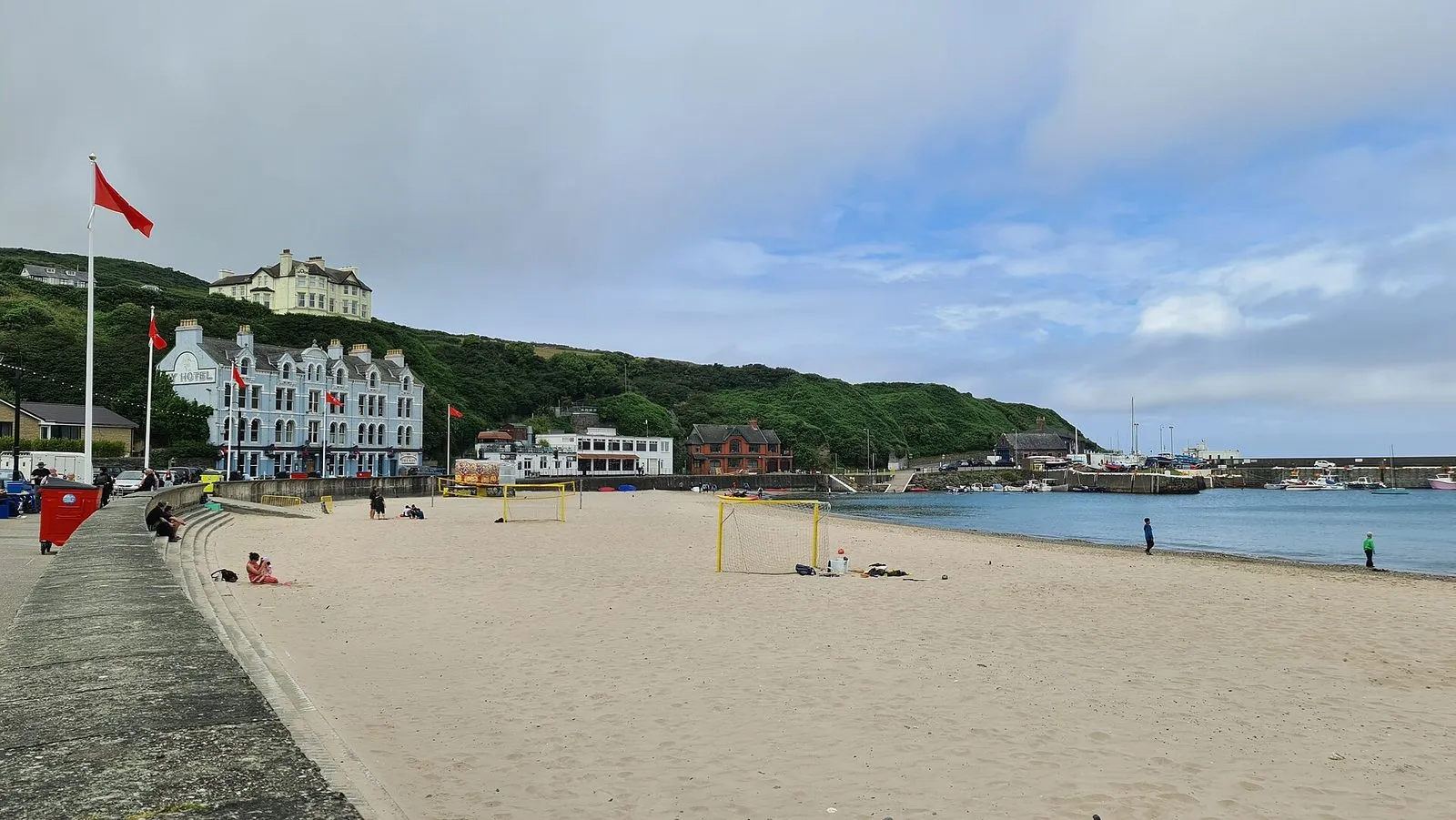 A wide sandy beach at Port Erin with goalposts on the sand, a white hotel on the hillside and the harbour breakwater beyond
