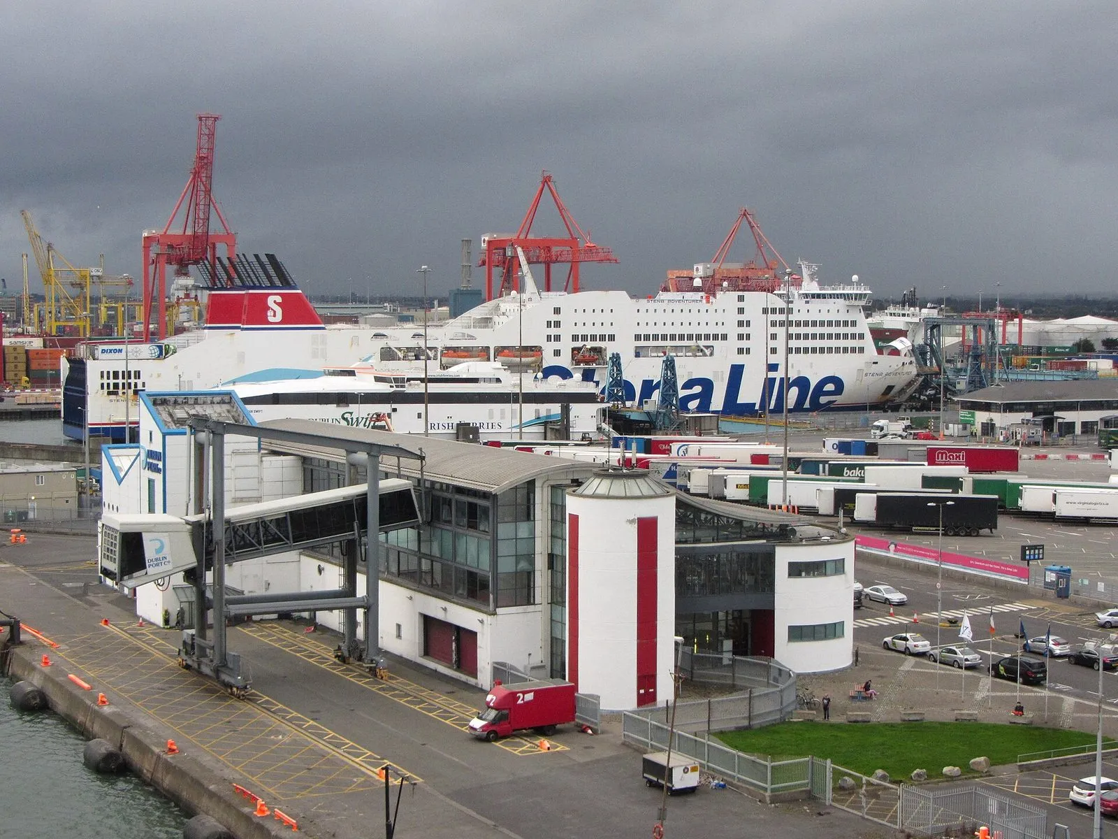 A white ferry terminal with a red and white round tower at Dublin Port, with a Stena Line ferry and red container cranes behind under a dark sky