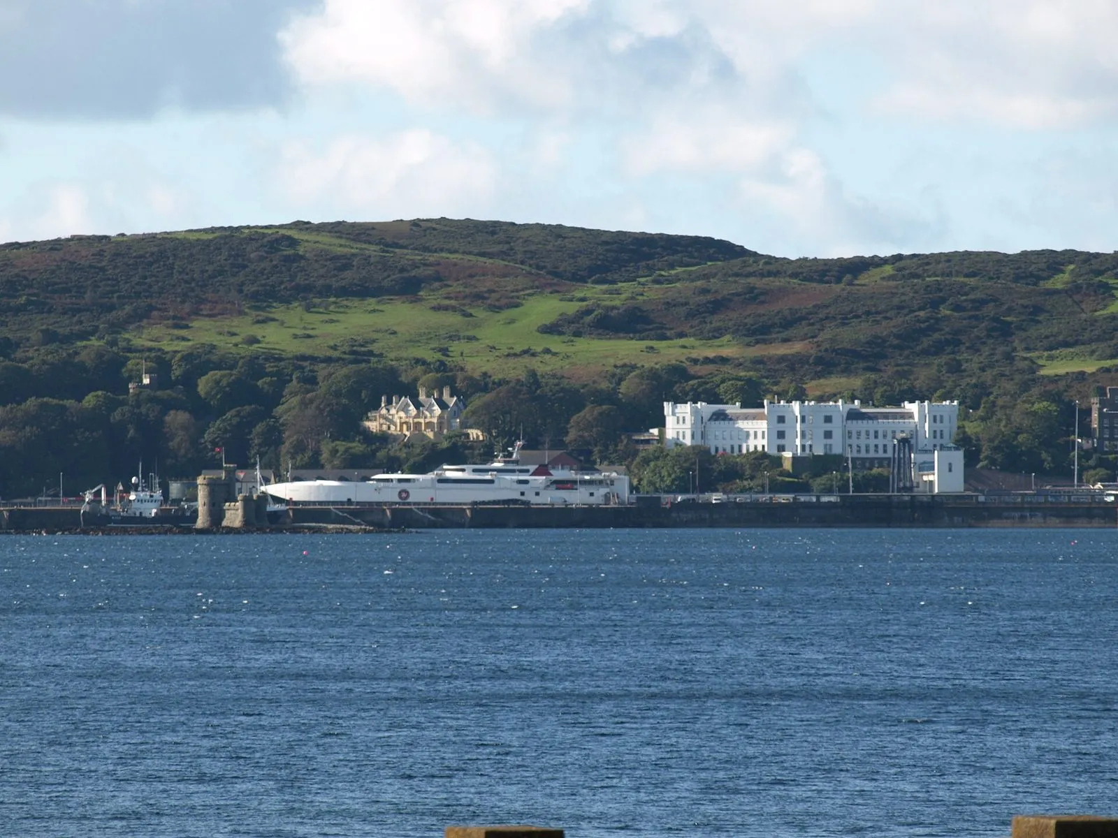 The fast craft Manannan, a long white catamaran, berthed in Douglas Harbour beneath Douglas Head