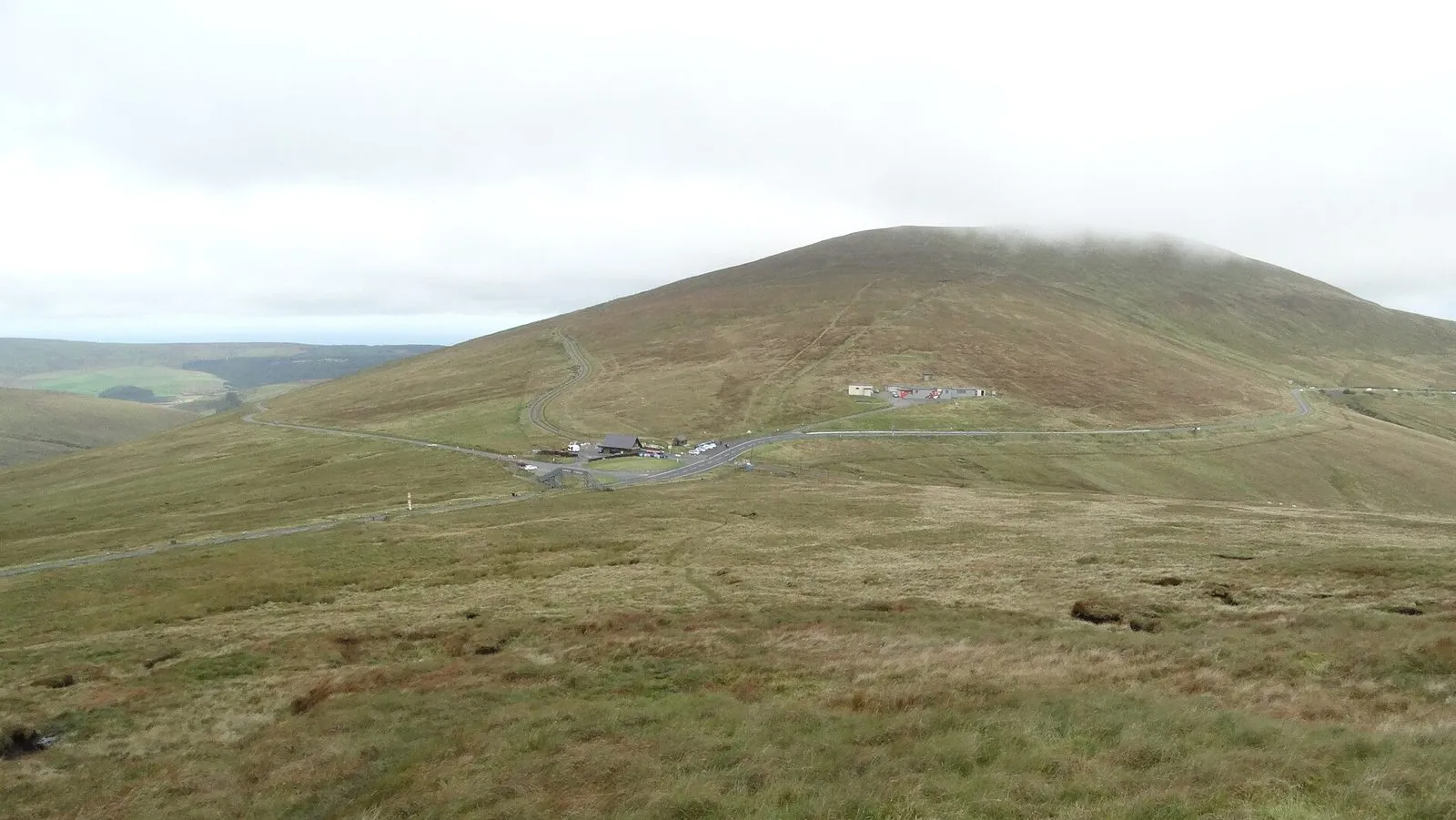 The Mountain Road crossing open brown moorland below the rounded summit of Snaefell, with the Bungalow buildings in the dip