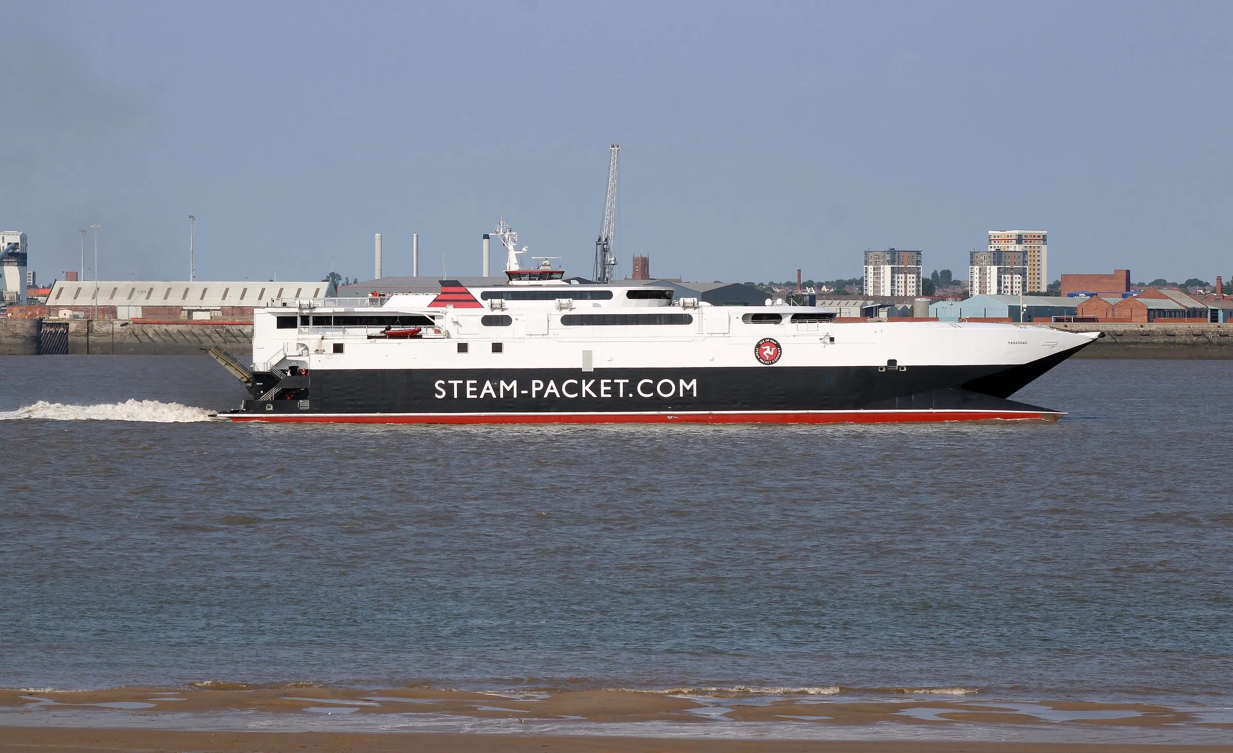 The Steam Packet fast craft Manannan, white with a black hull, crossing the Mersey past the Liverpool docks