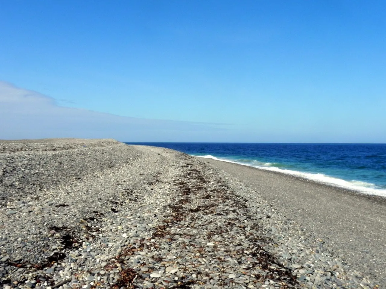 The long shingle beach at the Point of Ayre stretching away under a clear blue sky, with small waves breaking