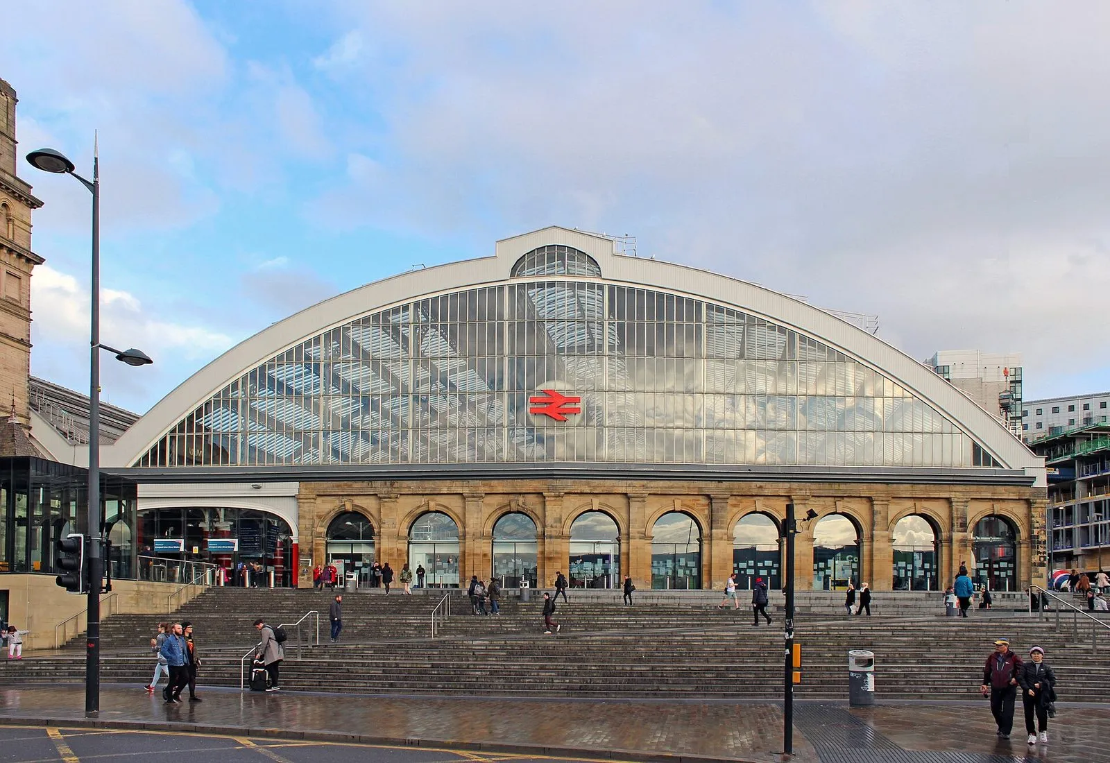 The glass arched roof and stone frontage of Liverpool Lime Street station, with people on the steps in front