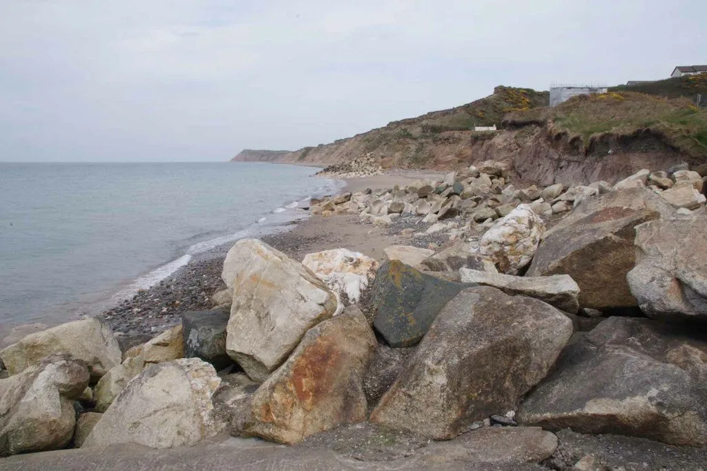 Grey boulders of rock armour on the shingle at Glen Wyllin beach, with the eroded cliffs running north towards Orrisdale Head