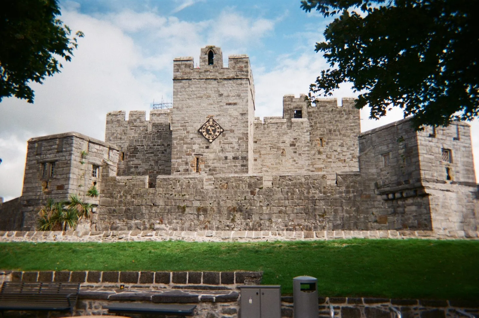 Castle Rushen’s grey limestone keep and towers behind a grassy bank, with the one-handed clock on the central tower