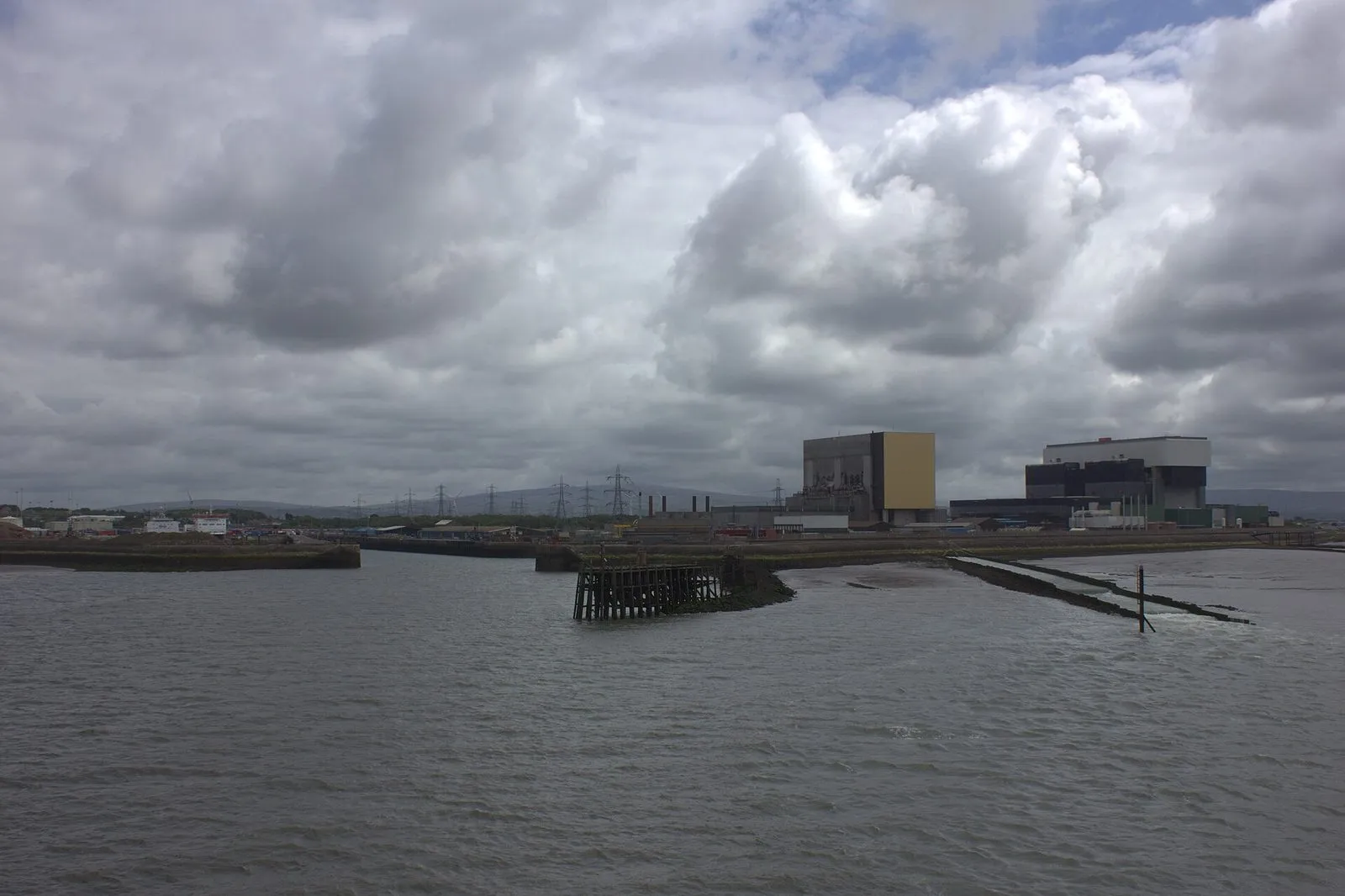 Heysham harbour seen from the sea under heavy grey cloud, with the two big block buildings of Heysham nuclear power station behind the quay
