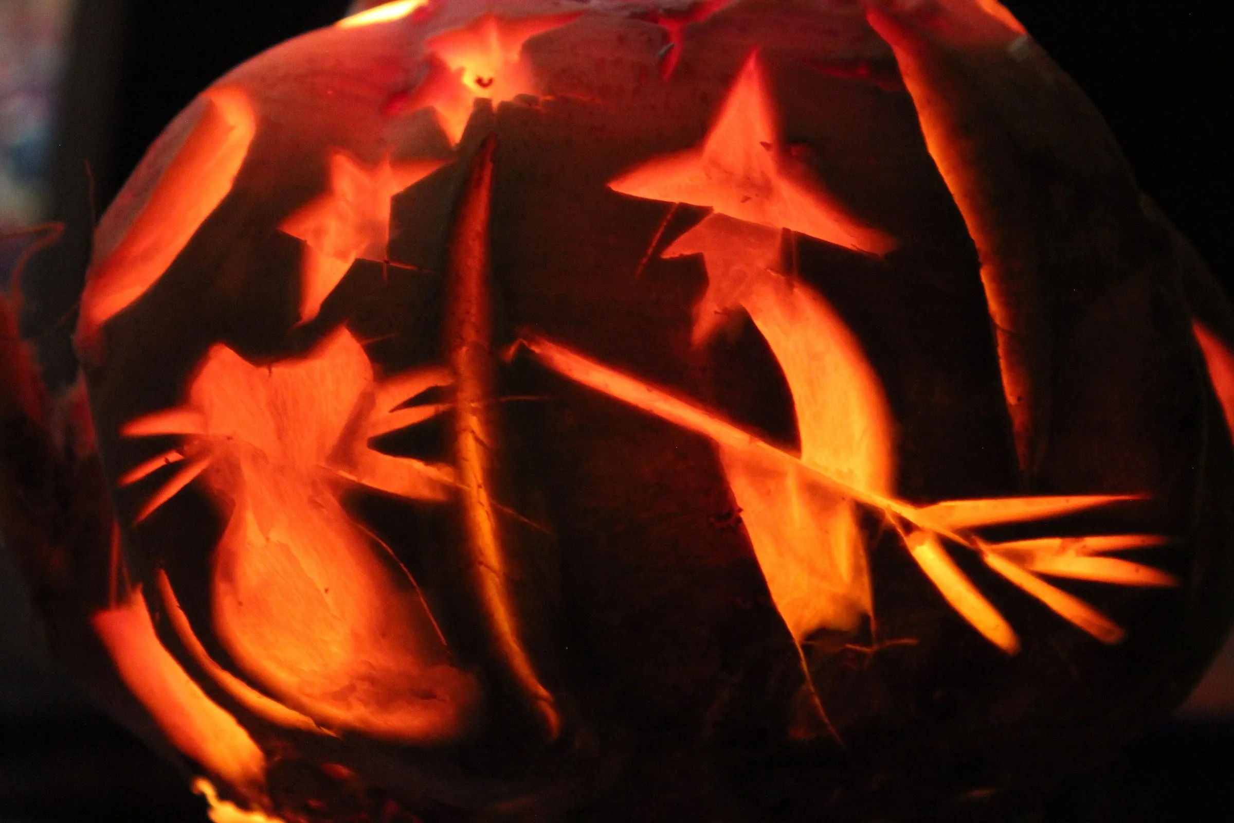 A carved turnip lantern glowing orange in the dark, showing a witch on a broomstick, a cat and stars