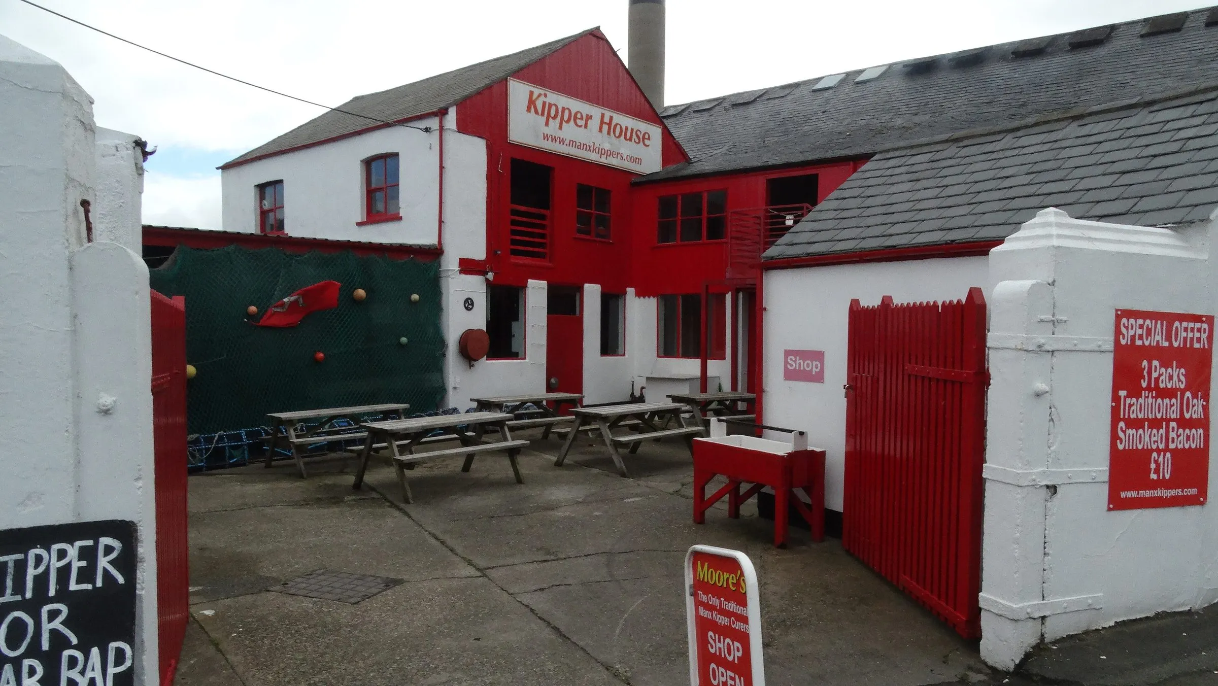 The red and white Kipper House on Mill Road in Peel, with picnic tables in the yard and a tall brick chimney behind