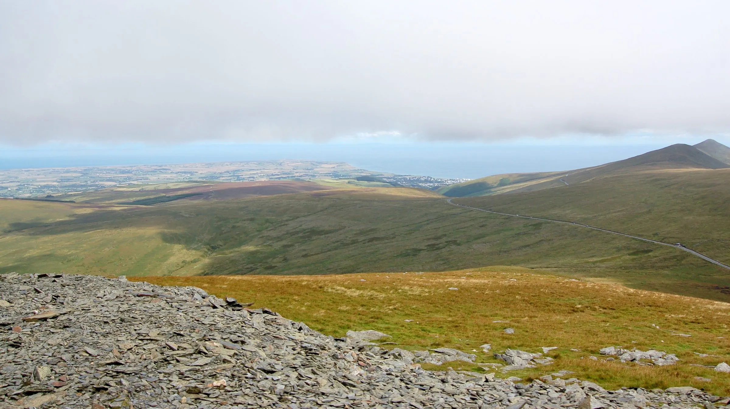The view north from the Snaefell Mountain Railway over moorland to the flat northern plain, Ramsey and the sea, with the Mountain Road curving across the hillside on the right