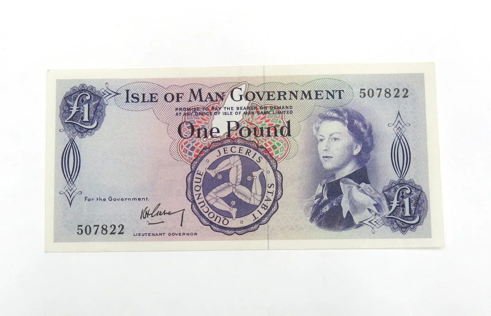 An older Isle of Man Government one pound note, blue and purple, with a portrait of the young Queen Elizabeth II and the three legs of Man in a circle