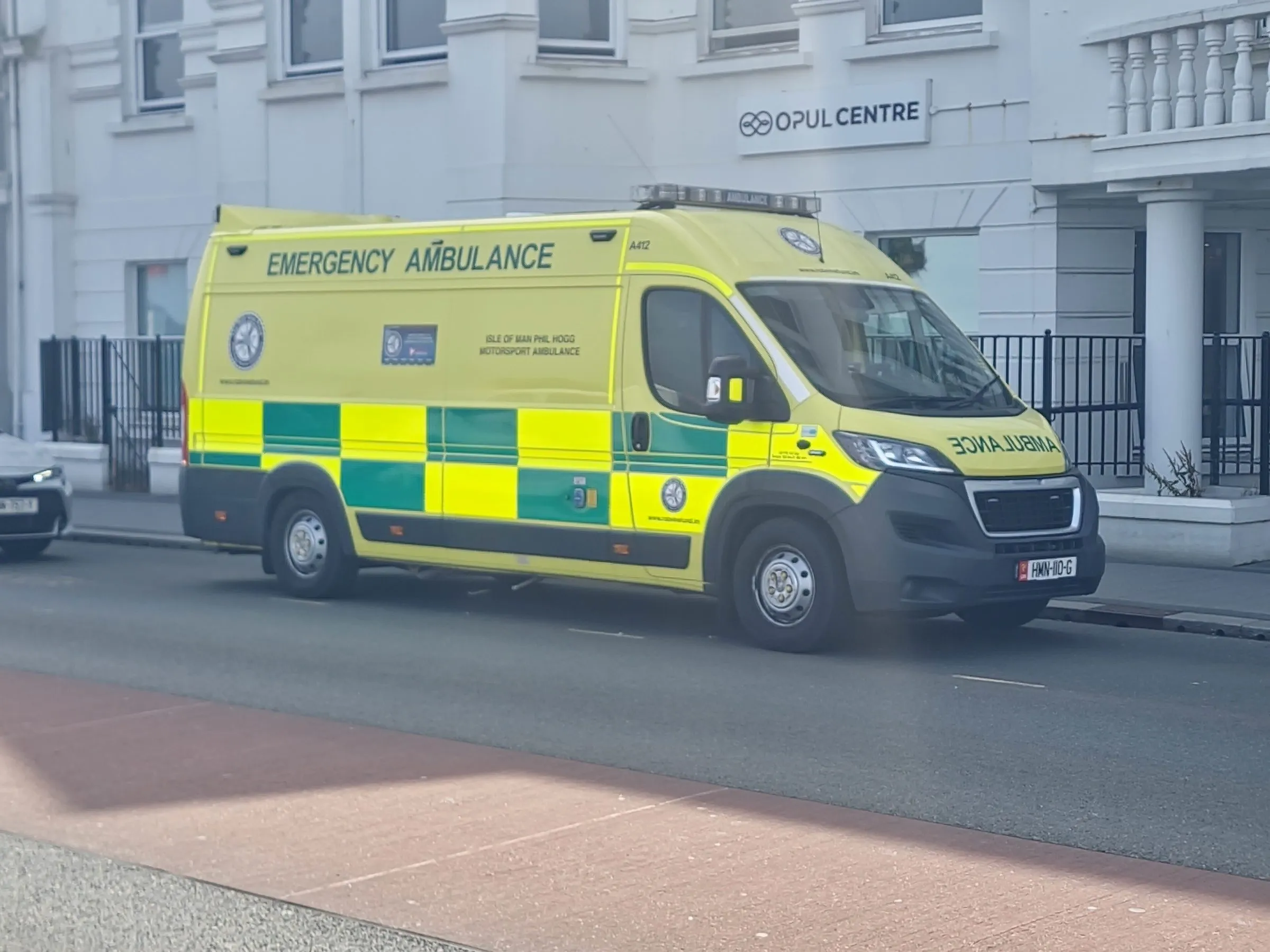 A yellow-and-green emergency ambulance with Isle of Man markings parked at the kerb of a town street