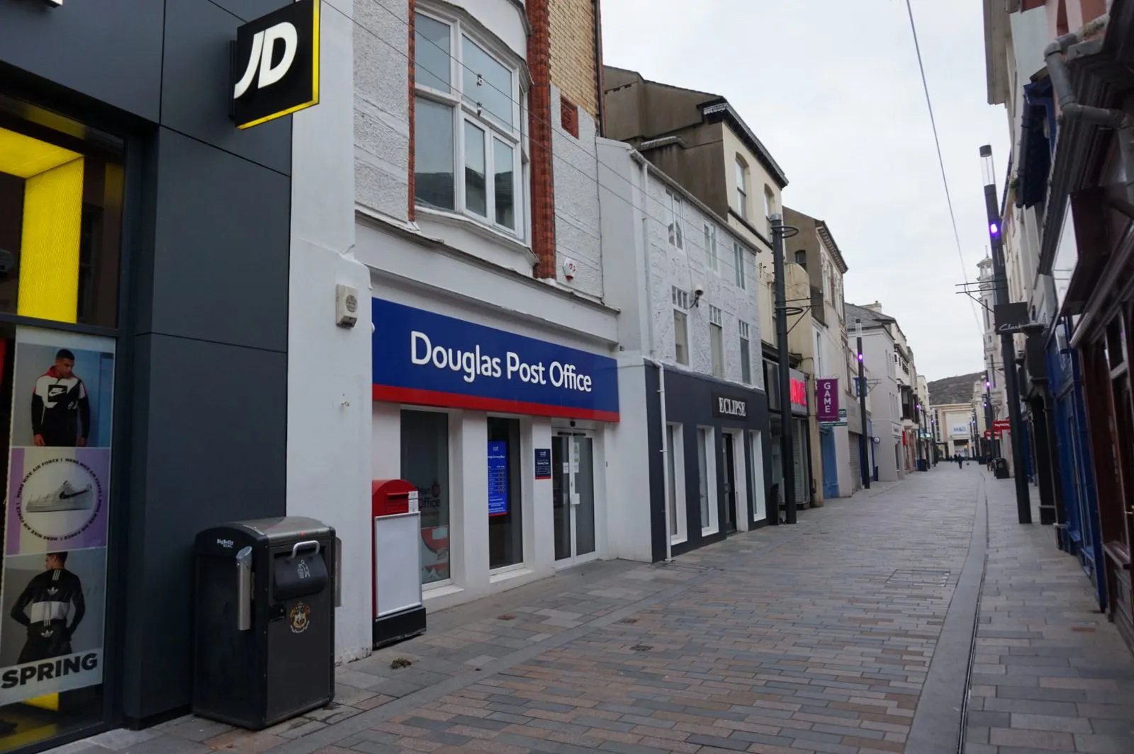 Douglas Post Office on Strand Street, with its blue sign and a red post box outside, looking down the pedestrianised shopping street