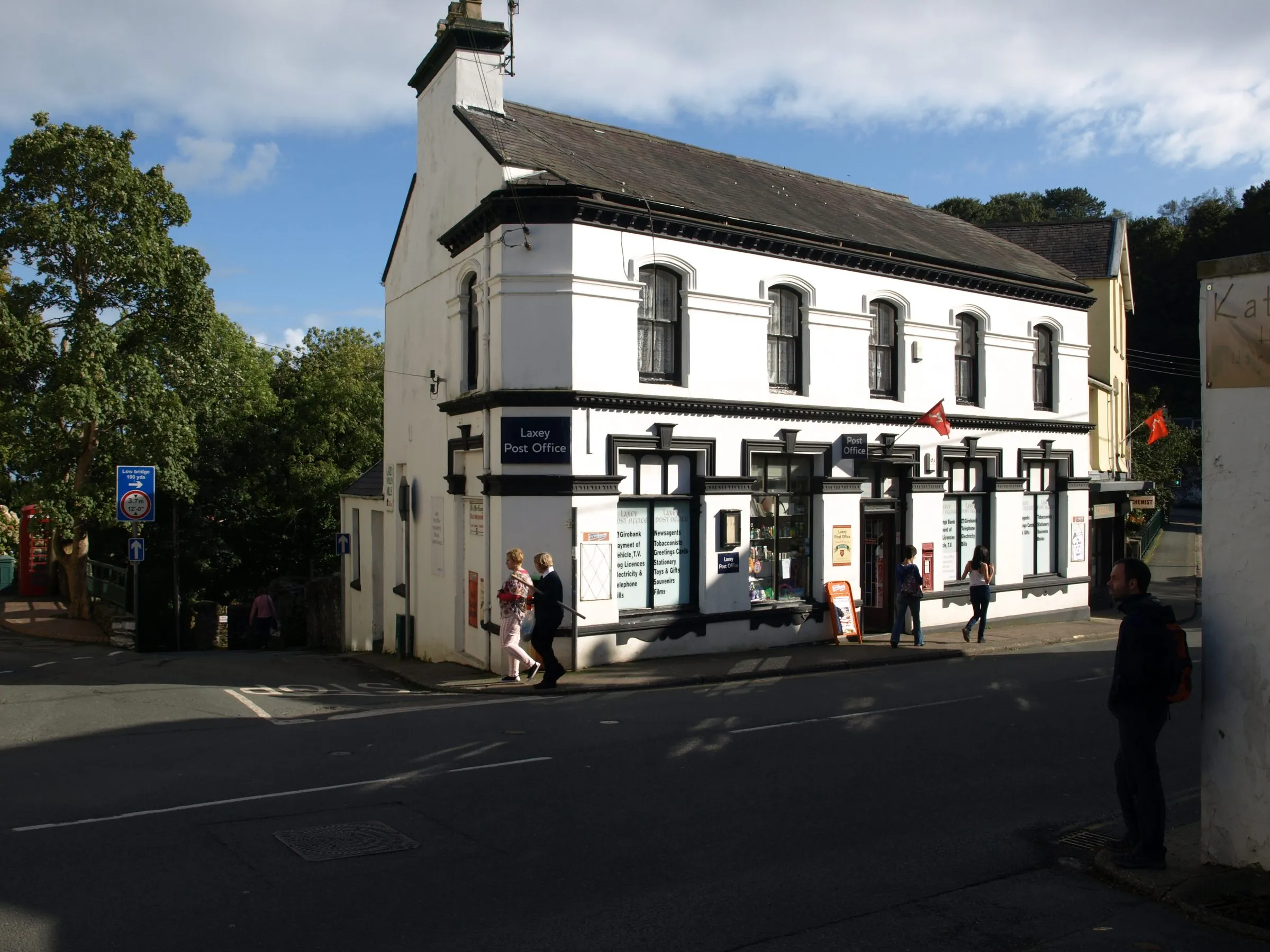 Laxey Post Office, a white two-storey building with black trim and a red Manx flag, on a sunny afternoon