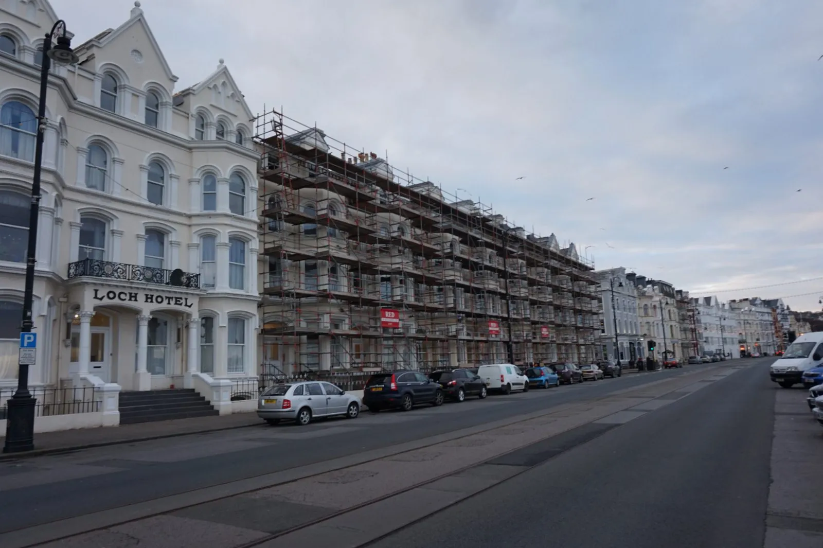 Cars parked along the kerb of Loch Promenade in Douglas, outside the white-painted Loch Hotel and a terrace covered in scaffolding