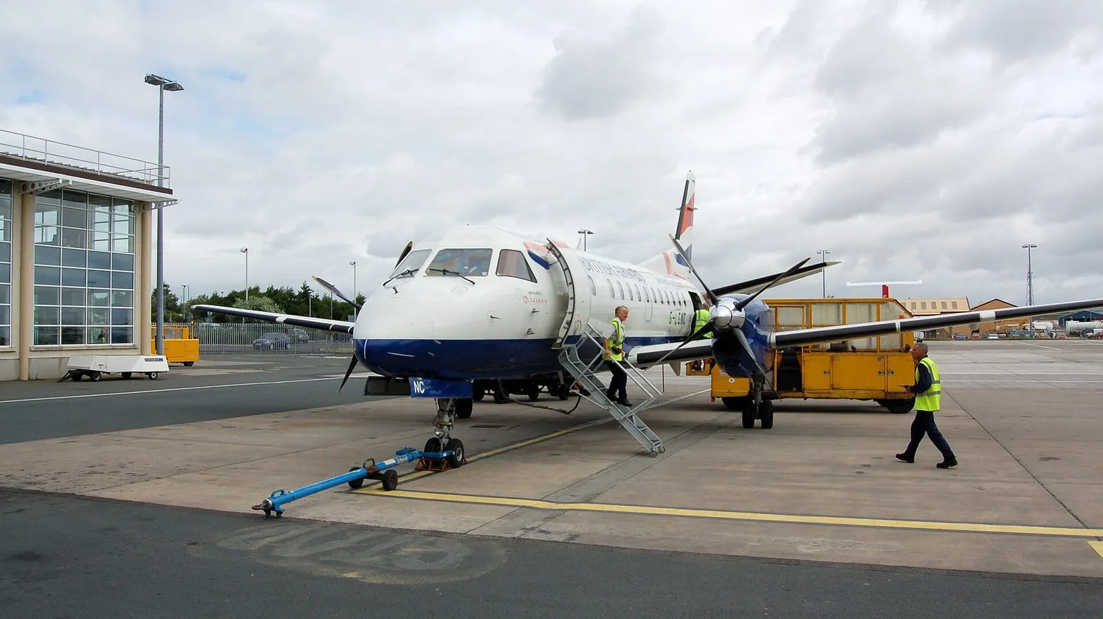 A small twin-propeller Loganair passenger plane parked on the apron at Ronaldsway, with steps down from its door and ground crew in hi-vis jackets