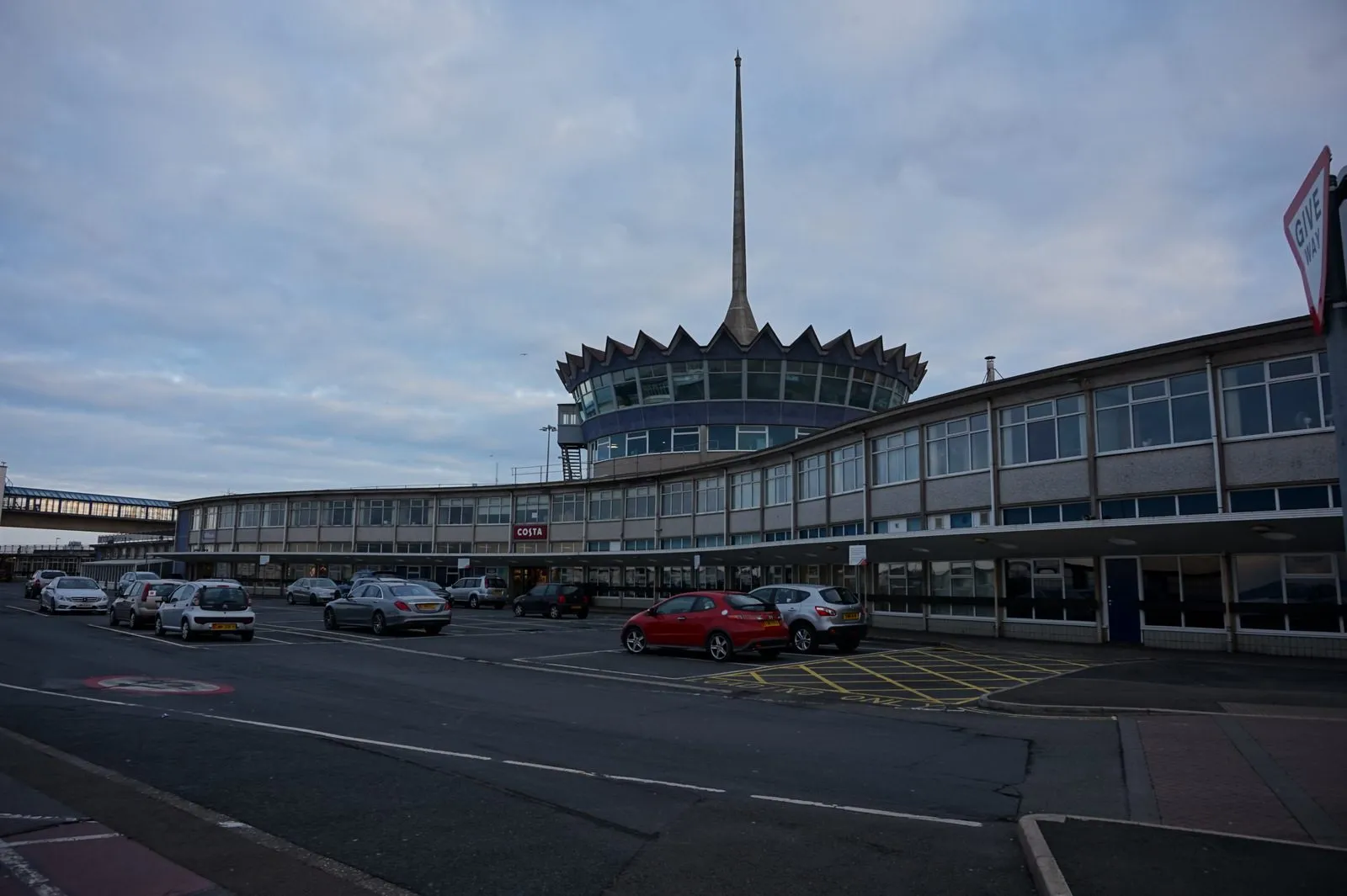 The Isle of Man Sea Terminal in Douglas, a curved two-storey building with a crown-shaped glass rotunda and a tall spire, with cars parked outside at dusk