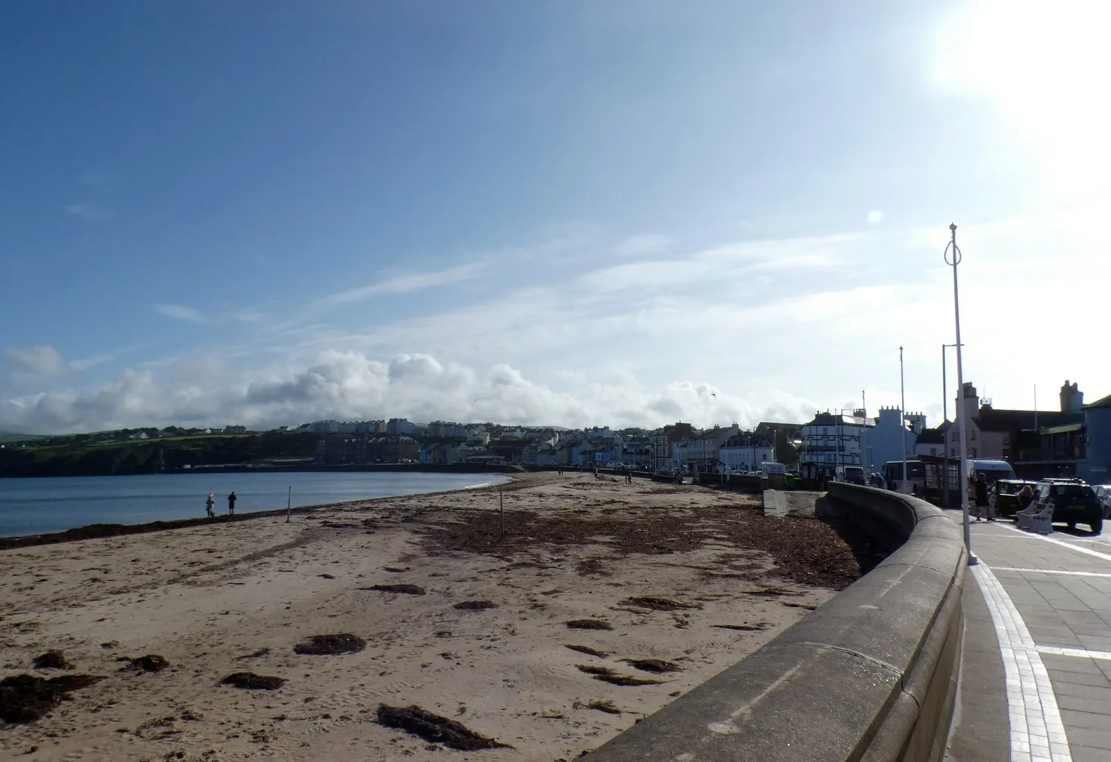 Peel promenade on a sunny day, the sandy beach and sea wall curving away towards the castle with the line of seafront houses on the right