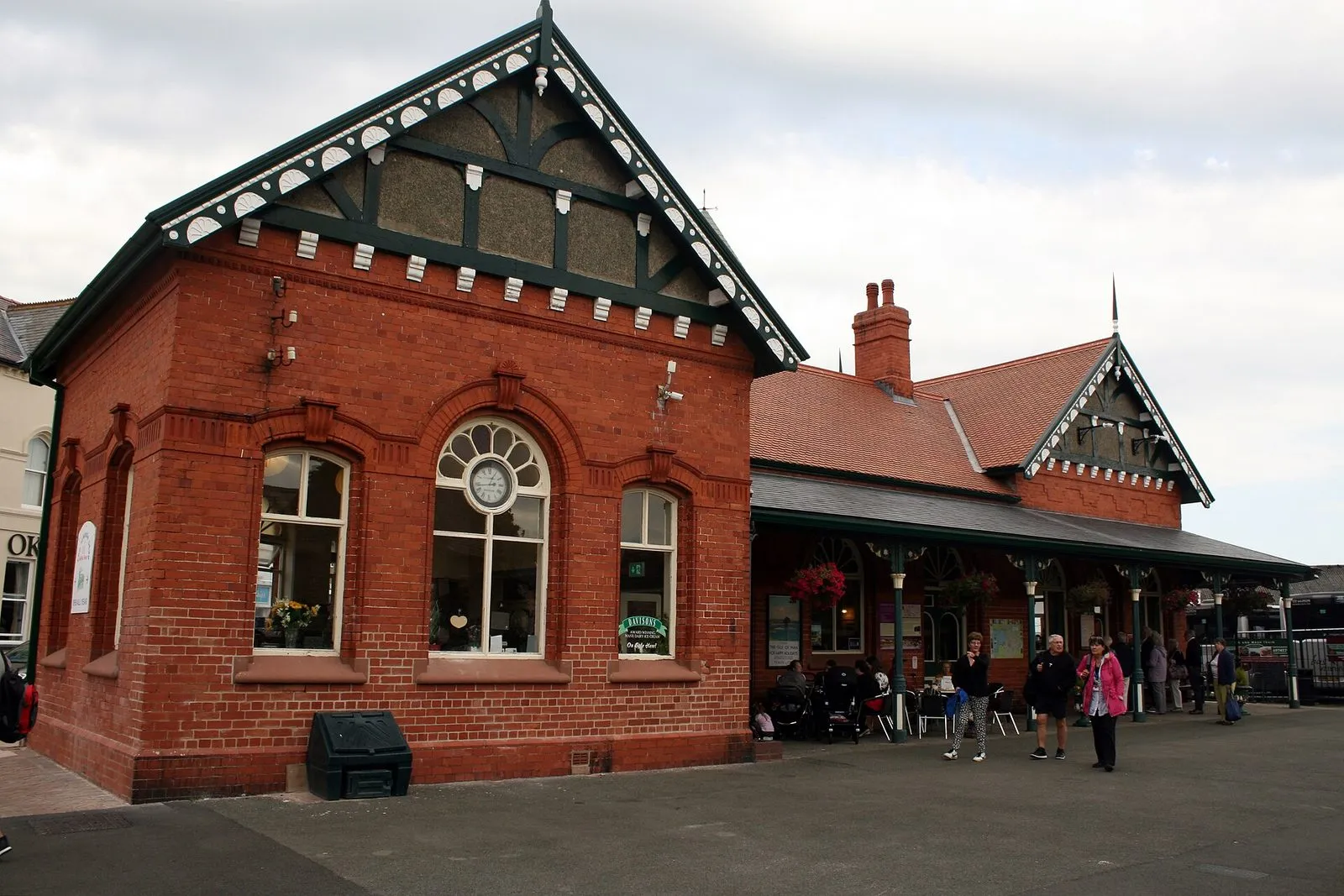 The red-brick Victorian station building at Port Erin with its ornate gables and a round window, people sitting at café tables outside