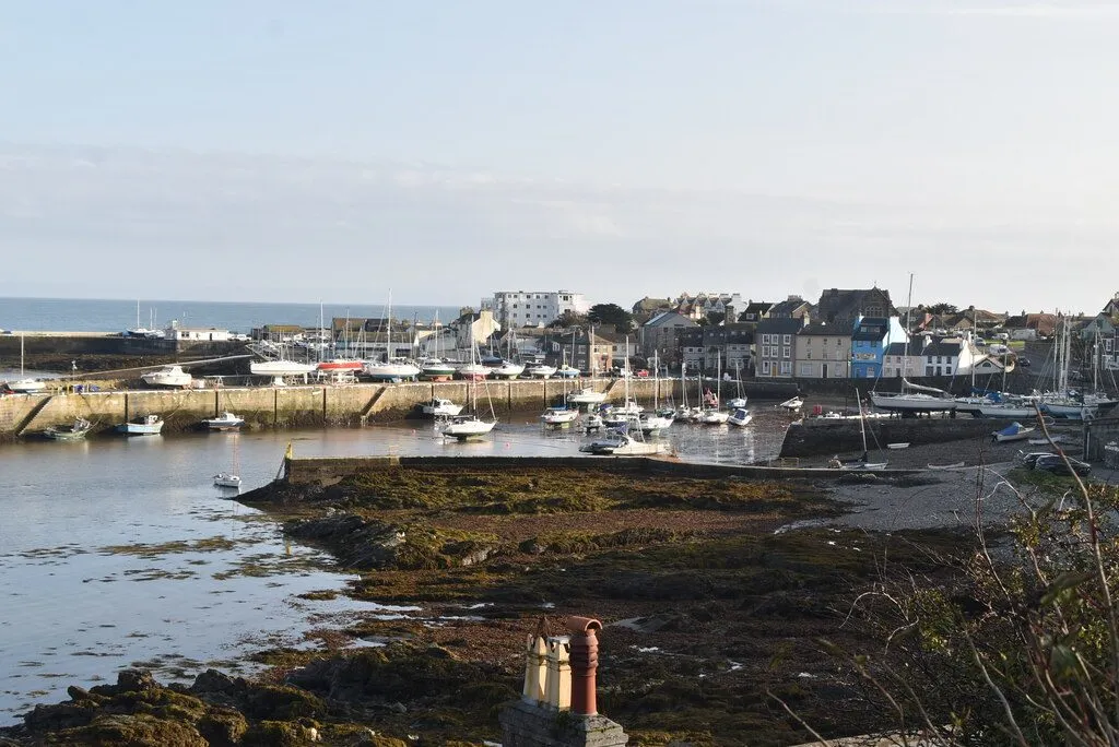 Port St Mary’s inner harbour at low tide, boats resting on the sand and weed behind the harbour wall, with the village’s white and pastel houses beyond