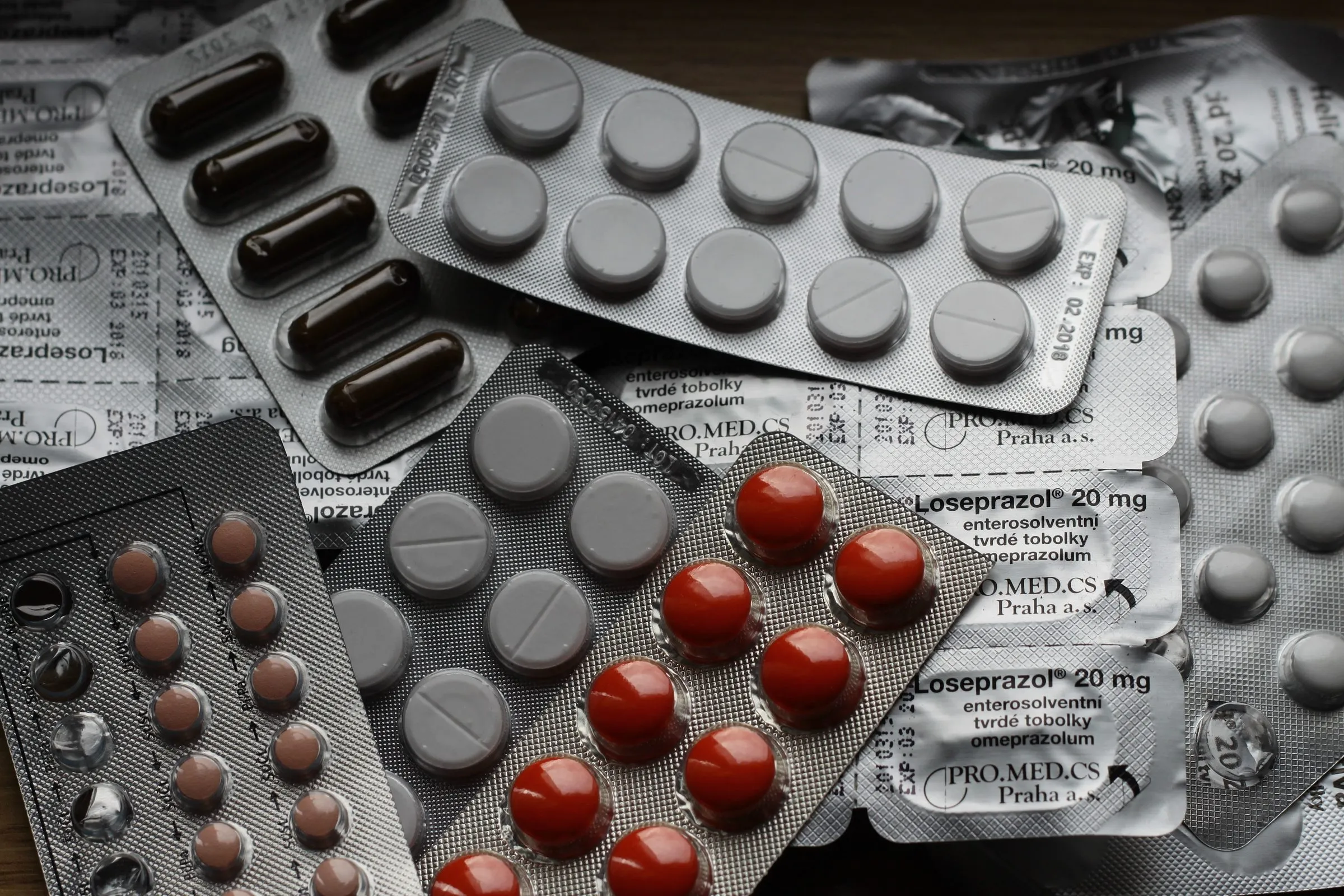 Blister packs of tablets and capsules piled on a wooden table