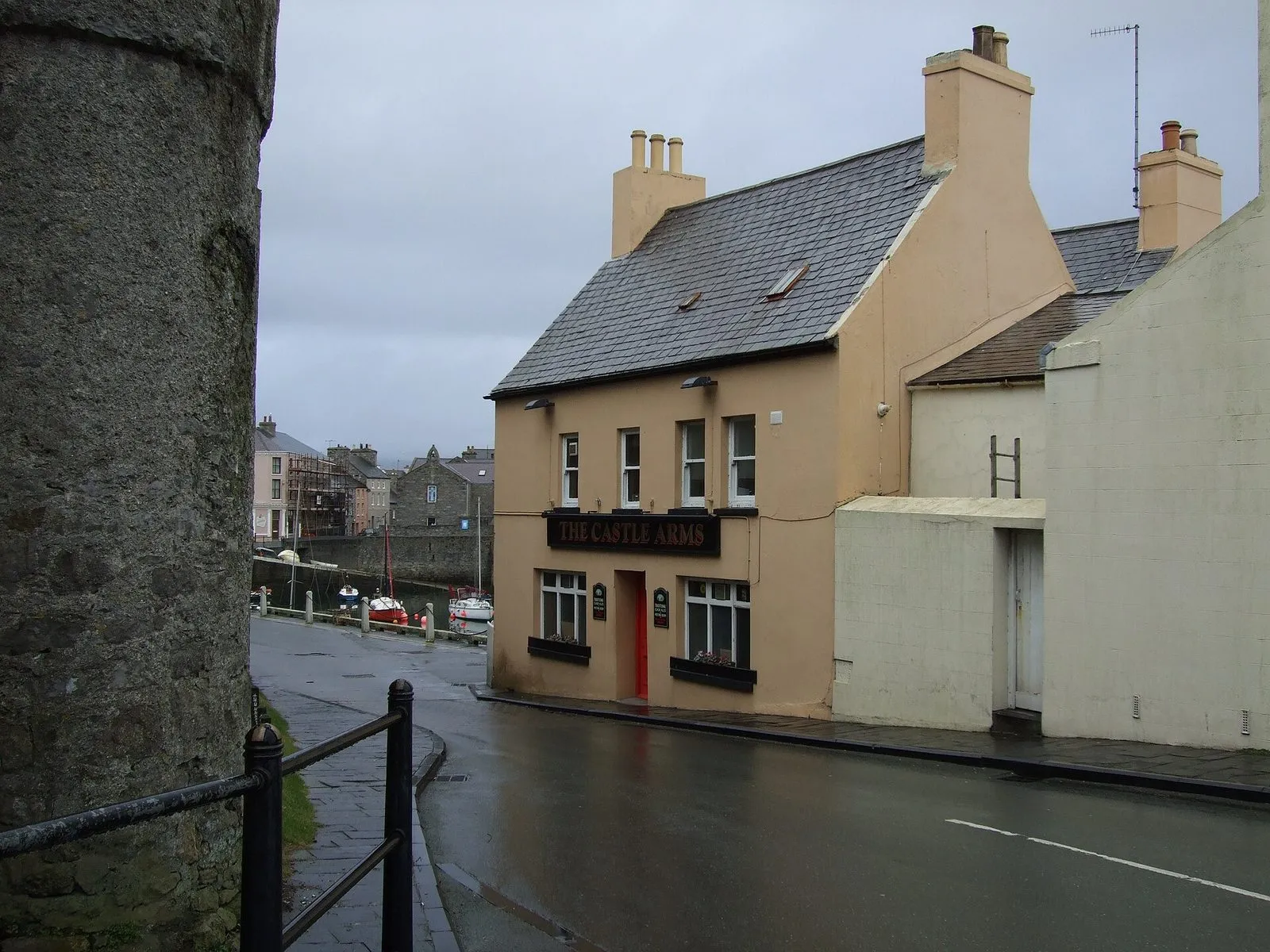 The Castle Arms, a small peach-painted pub on a corner by Castletown harbour, with the grey stone of Castle Rushen’s wall on the left