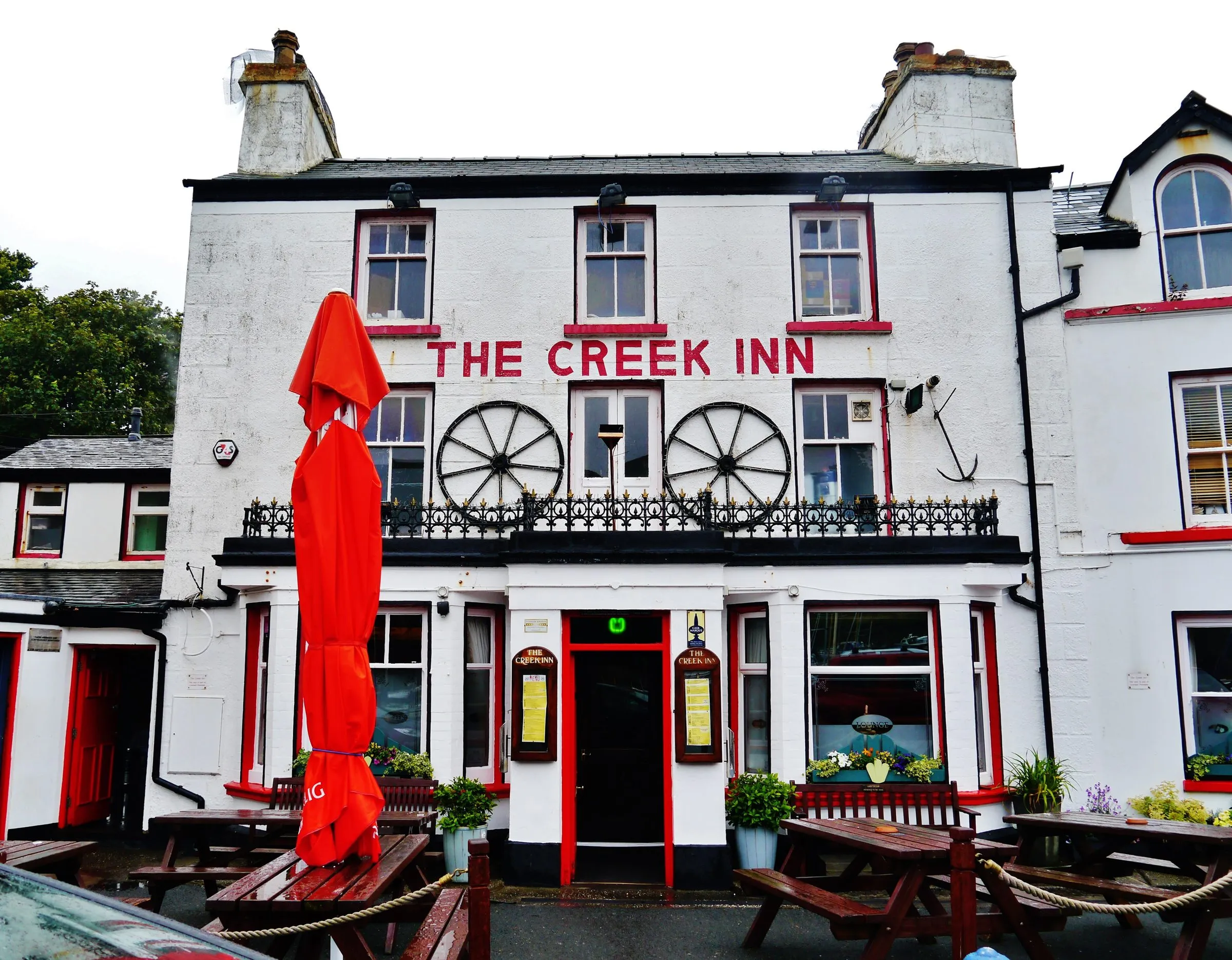 The white-painted Creek Inn on Peel's quayside, with red lettering, cartwheels on the balcony and picnic benches outside