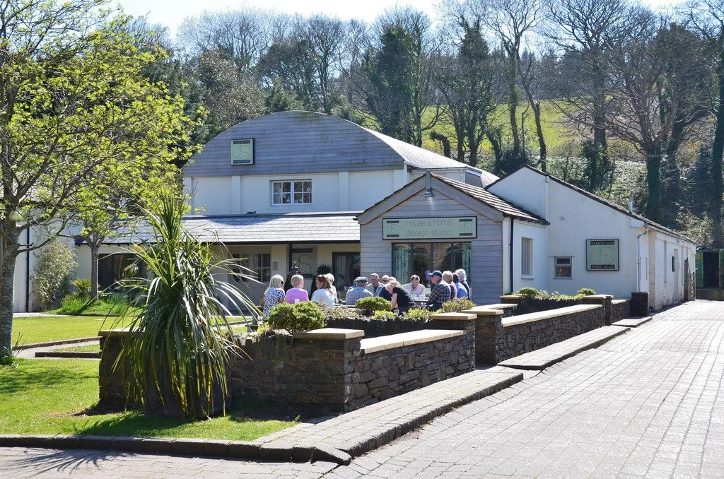 Shoppers sitting outside the cafés at Tynwald Mills, a group of low white converted mill buildings among trees