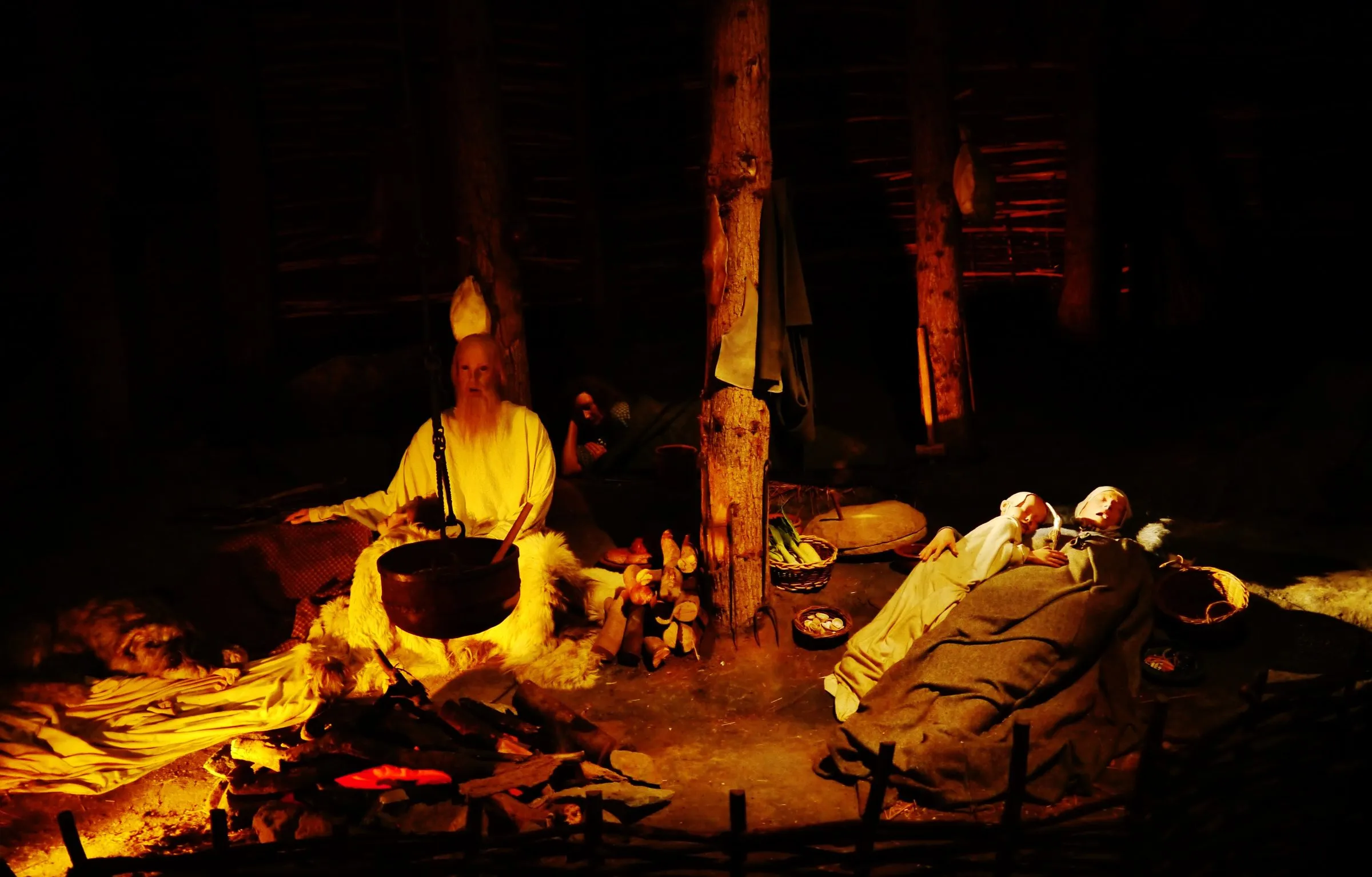 A firelit reconstruction of a Celtic roundhouse inside the House of Manannan, with figures sitting round a cooking pot