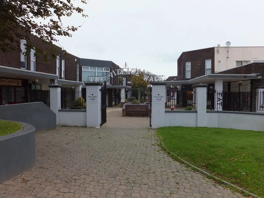 The gated entrance to The Village Walk in Onchan, a paved precinct of low 1970s brick buildings under a grey sky