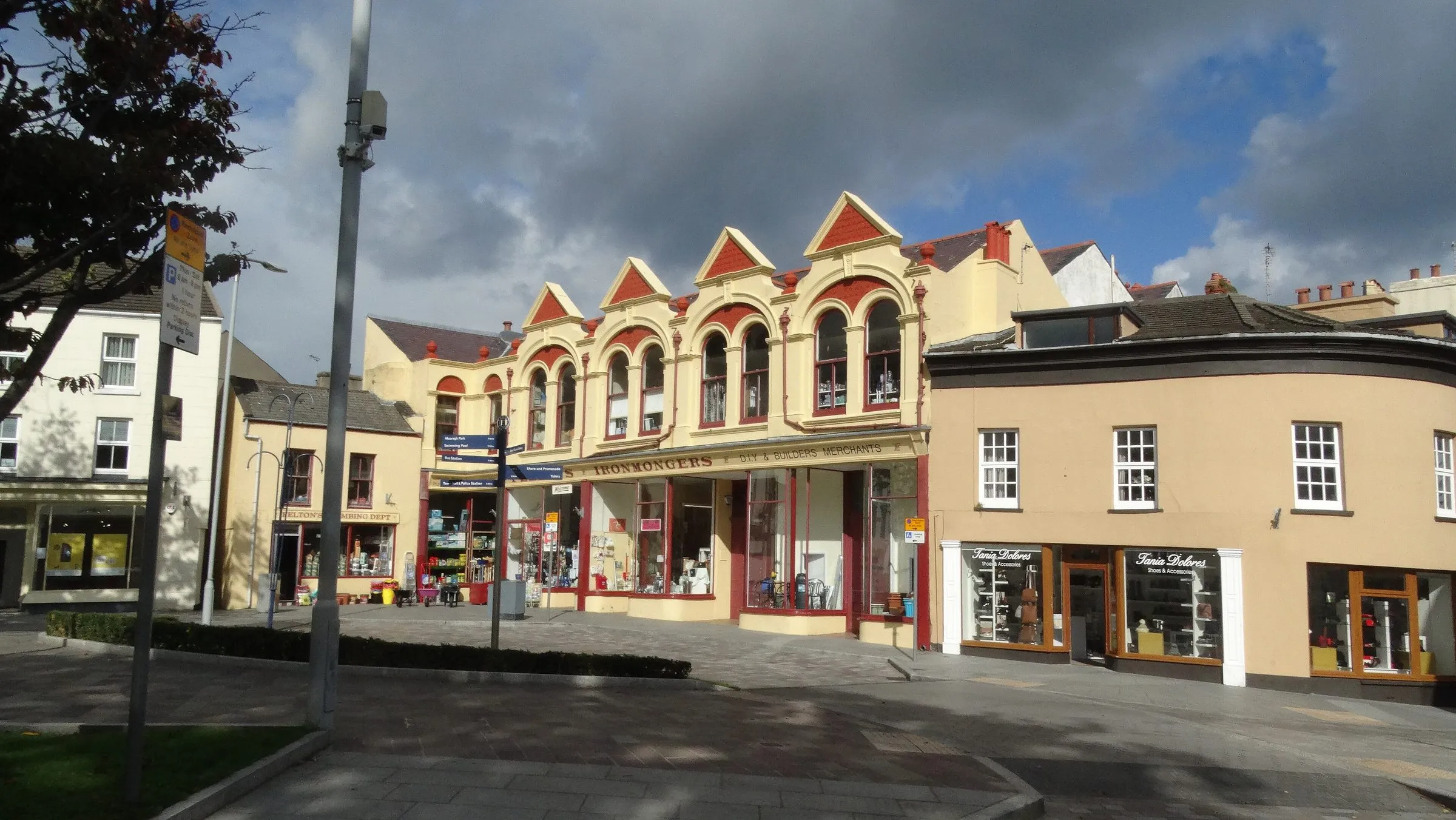Victorian shopfronts with red-trimmed gables on Parliament Street in Ramsey, under a cloudy blue sky