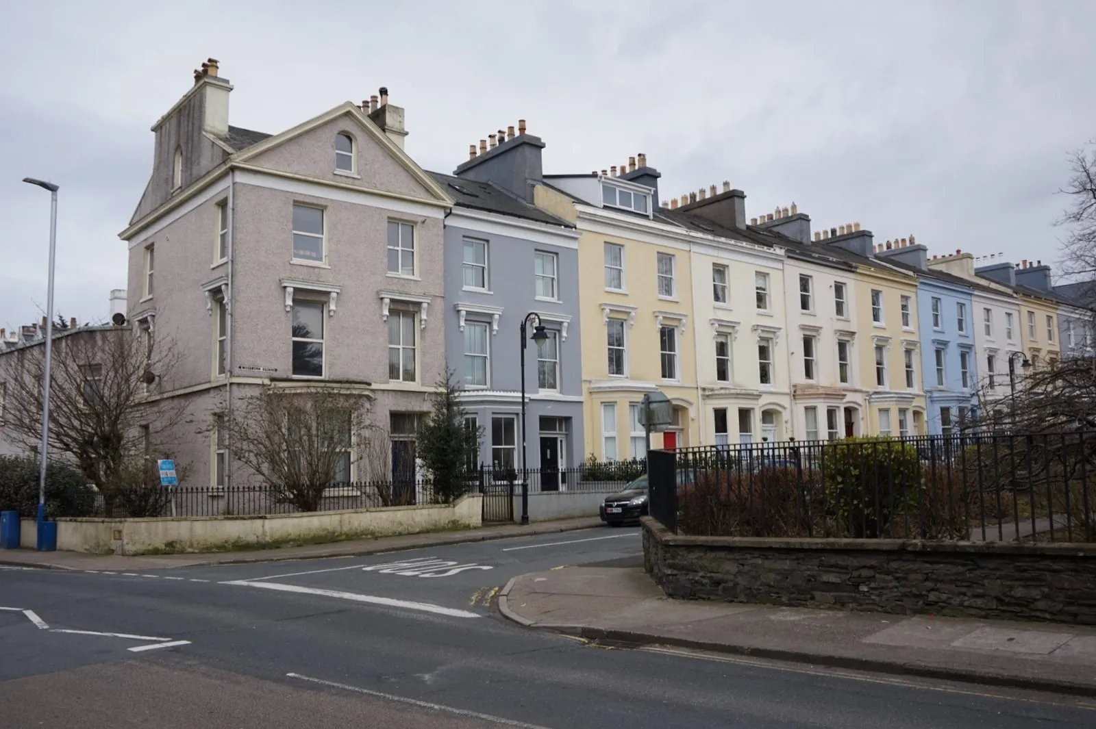A row of tall Victorian townhouses painted pink, grey, cream and blue on Woodbourne Square in Douglas