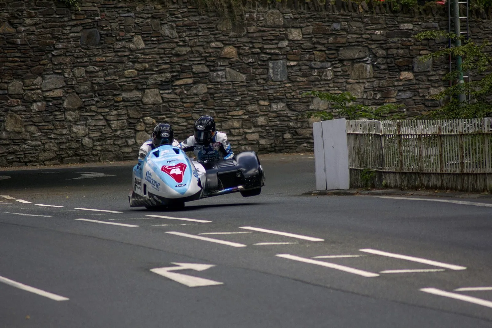 A sidecar outfit taking the left-hand bend at Braddan Bridge on the closed course, in front of a high stone wall