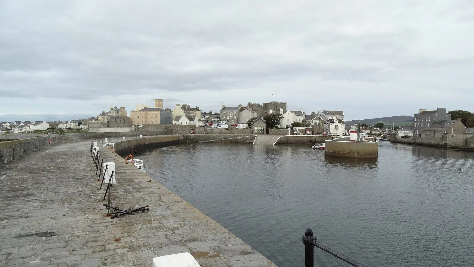 The inner harbour at Castletown on a grey day, with the stone quay curving round to the town’s houses and the castle’s tower behind