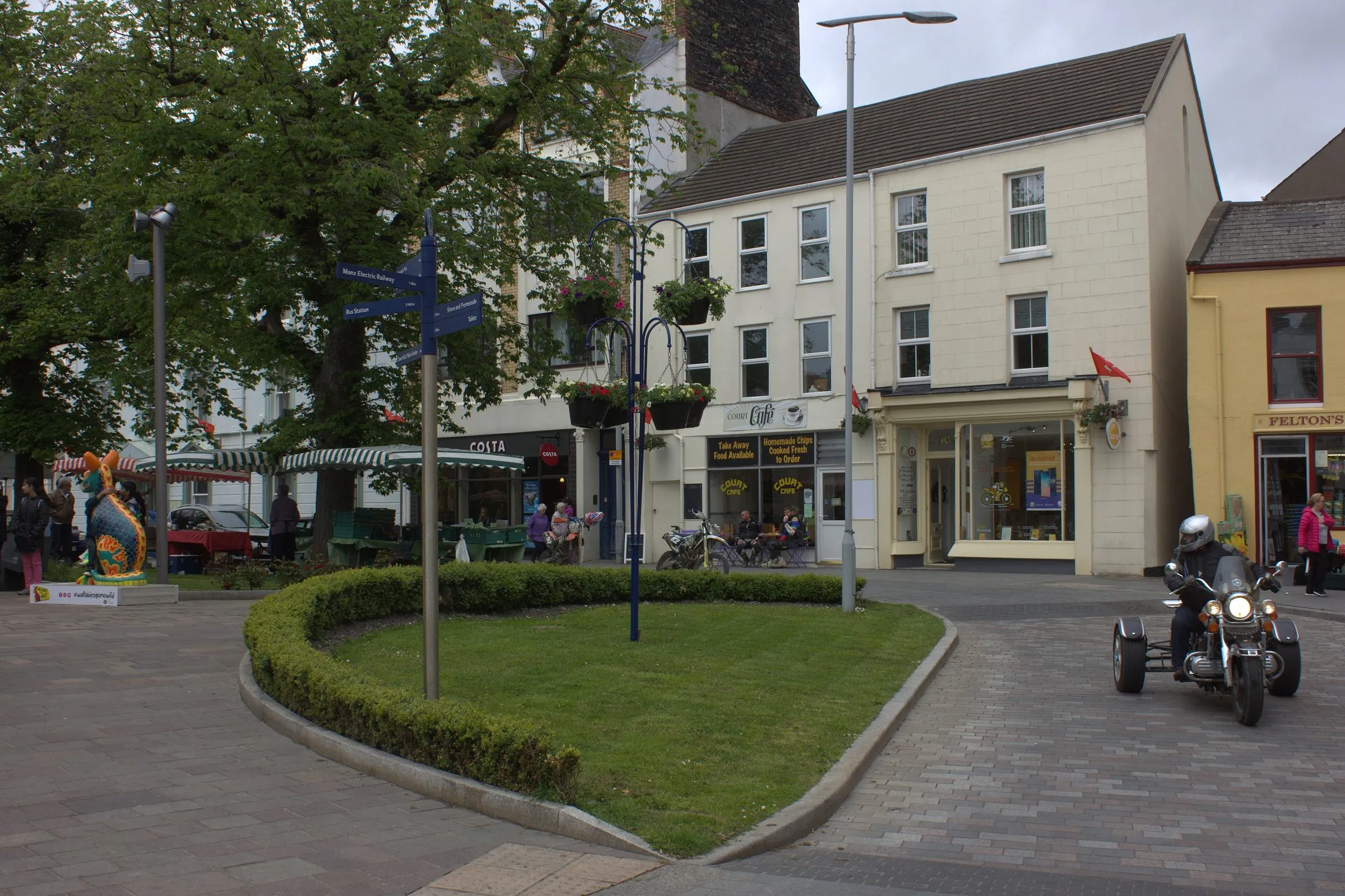 Ramsey town centre on an ordinary day, with a small green, a signpost, a café and shops in painted three-storey buildings