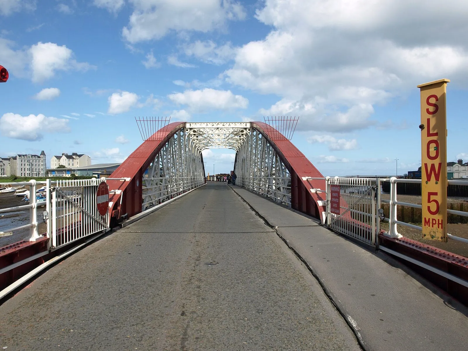 Looking across Ramsey’s red-and-white iron swing bridge over the harbour, with a yellow SLOW 5 MPH sign and white terraces beyond